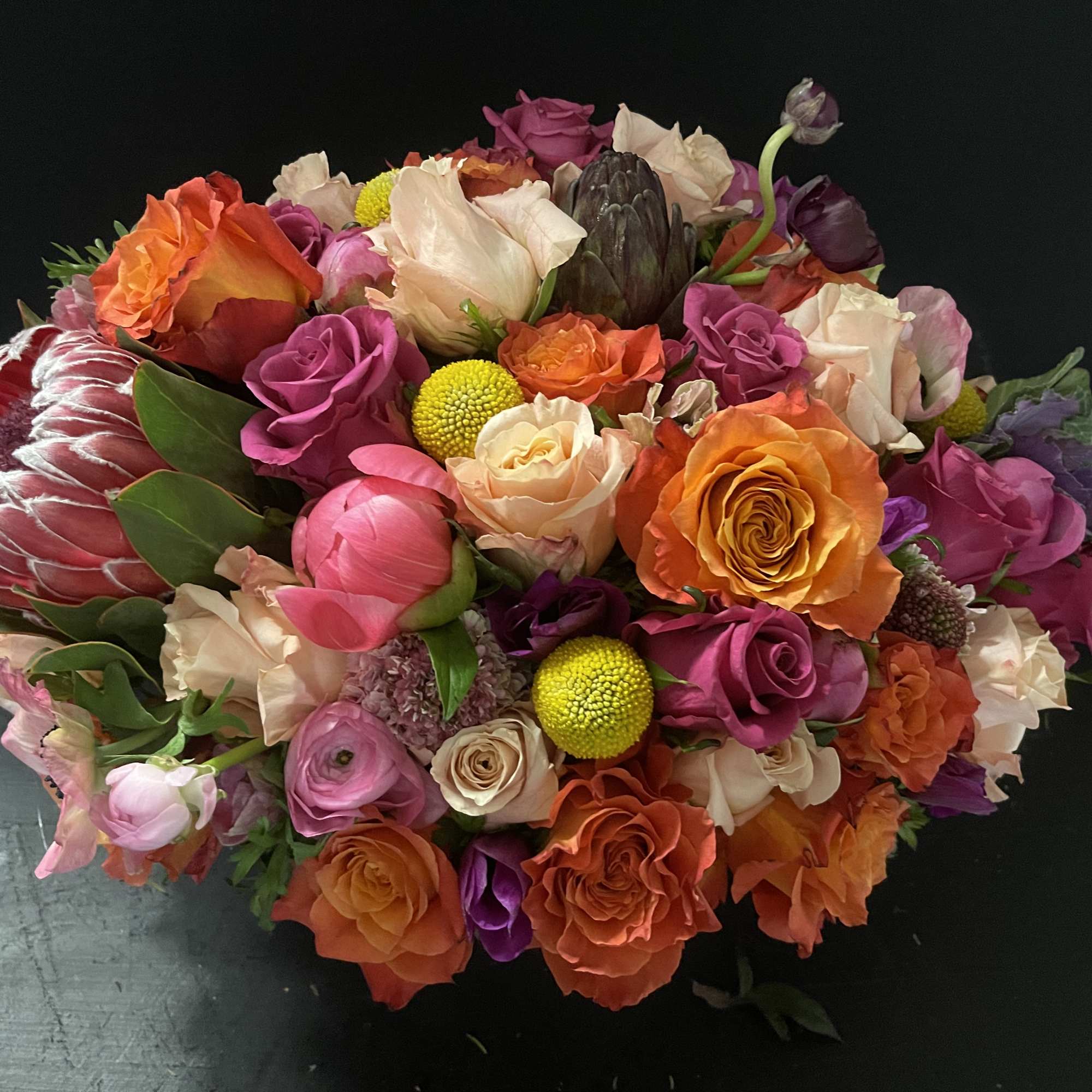 Lush hand-tied bouquet of orange, pink, and peach flowers with protea and roses.