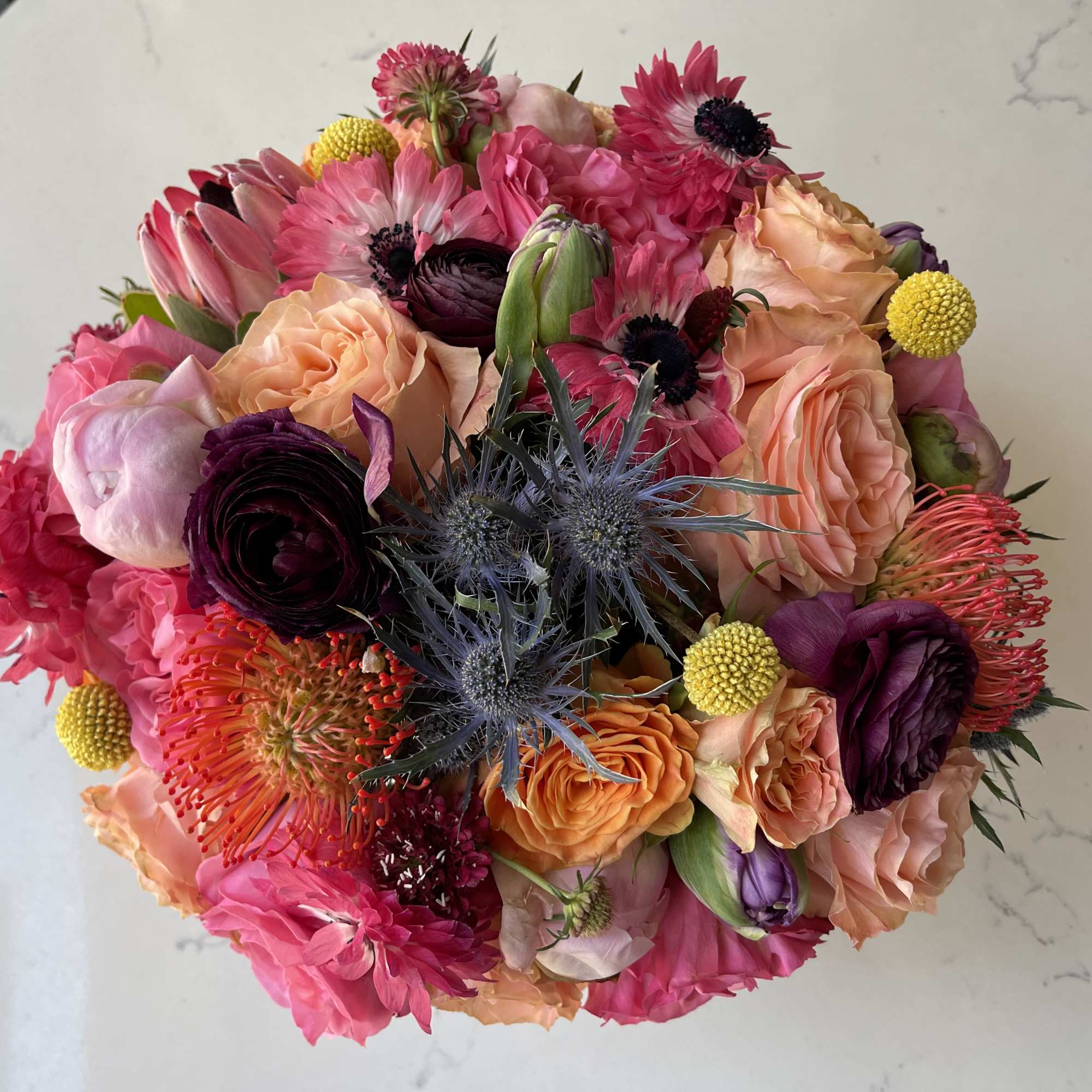 Round mixed bouquet of pink and peach blooms with purple and yellow accents viewed from above