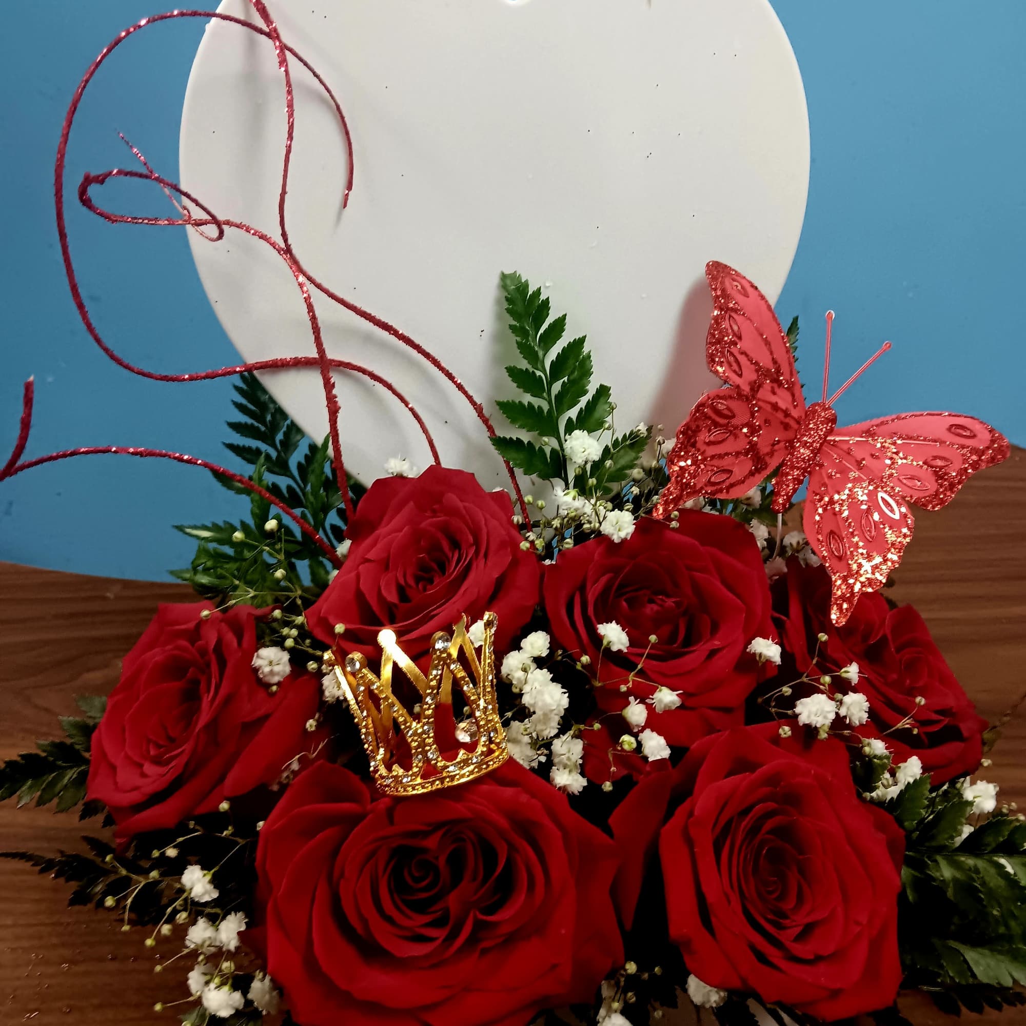 Red roses arranged with baby's breath and a butterfly topper in a heart-shaped backing