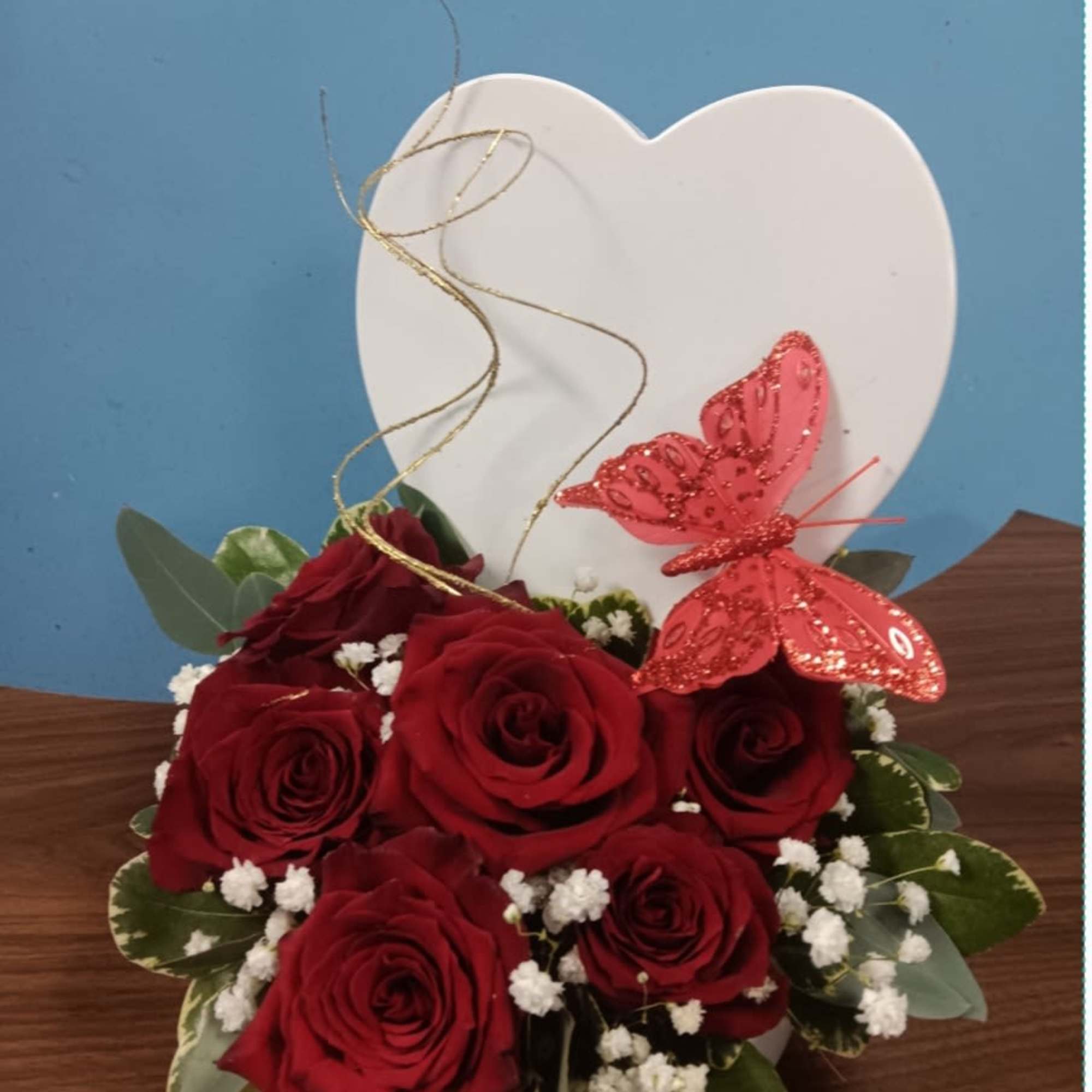 Red roses in a white heart-shaped box with a decorative butterfly topper
