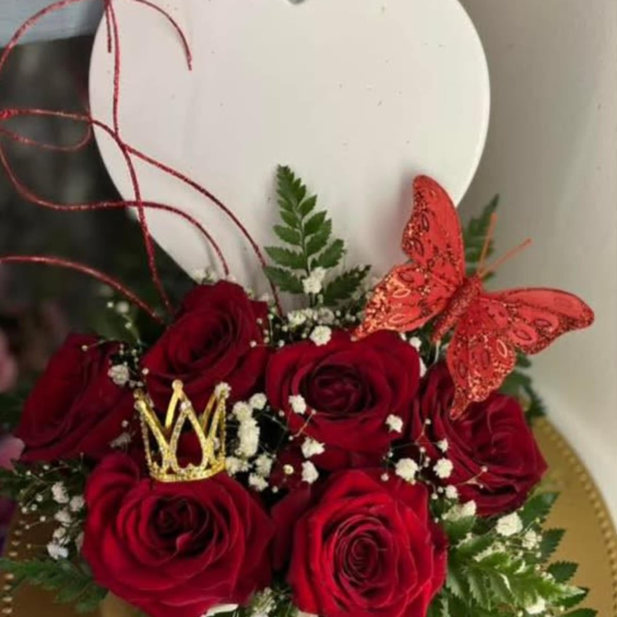 Red roses arranged with a gold crown and red butterfly in a heart-shaped box
