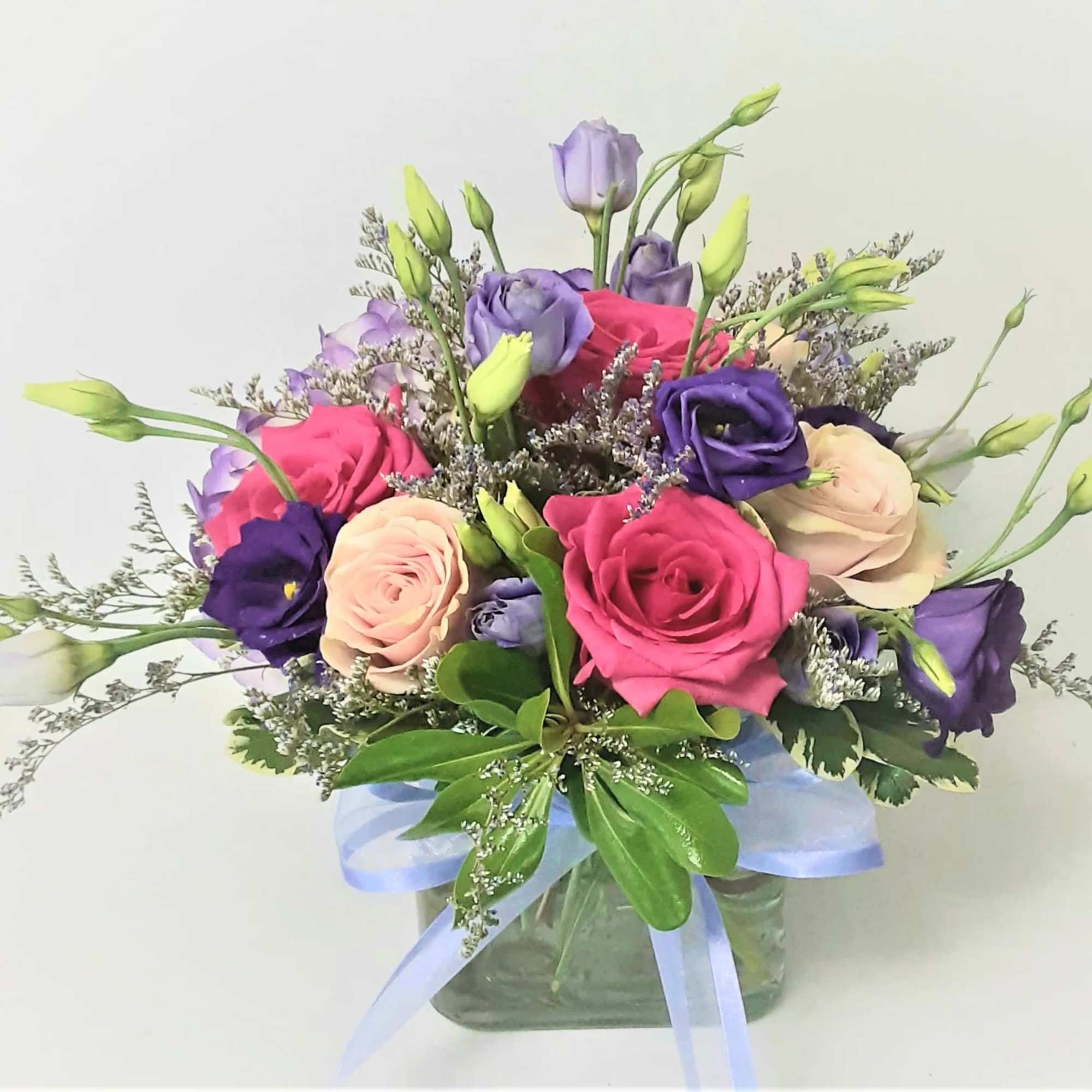 Pink, purple, and cream flowers in a glass vase with a blue ribbon