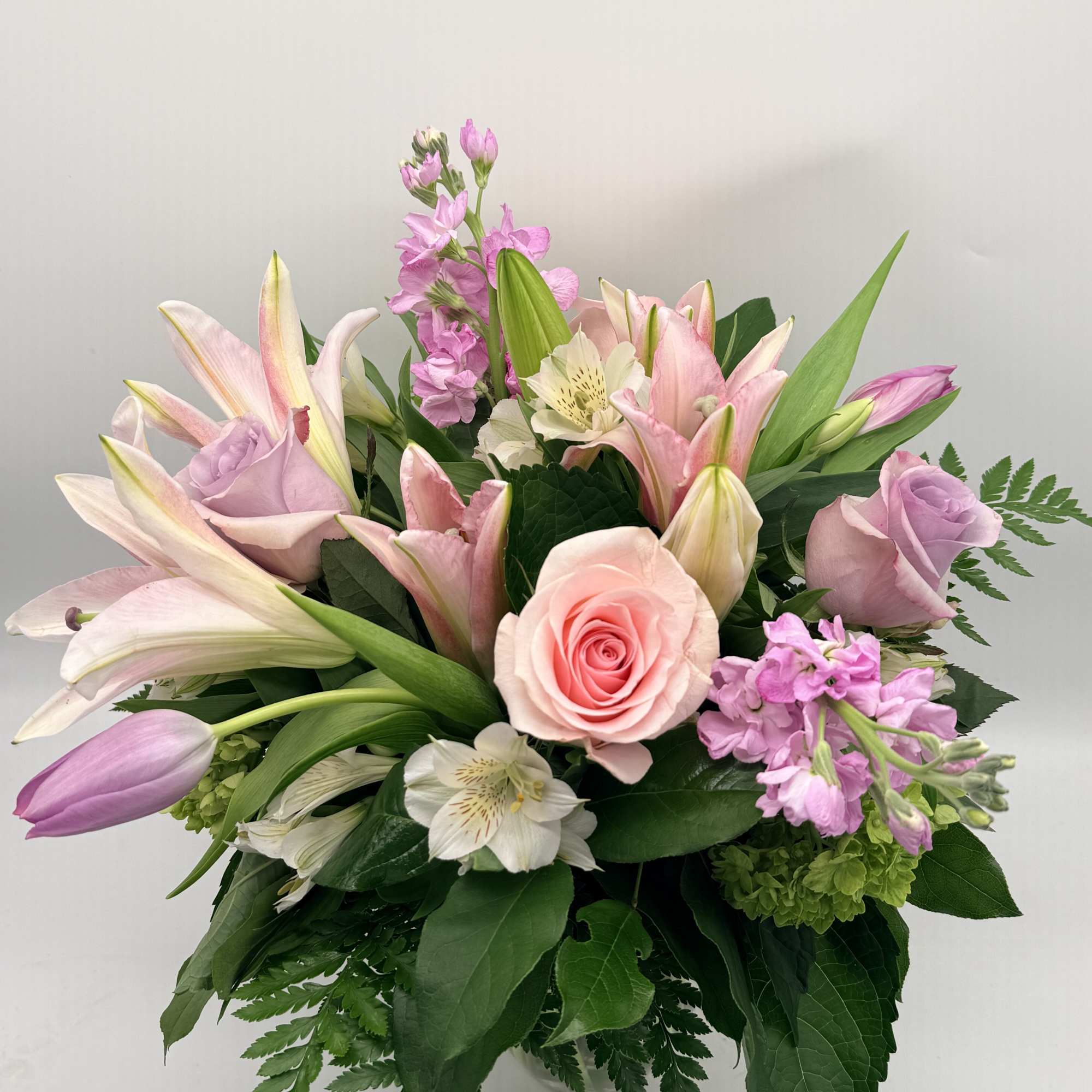 Soft, romantic, and effortlessly graceful, this garden-style arrangement features  lilies, roses