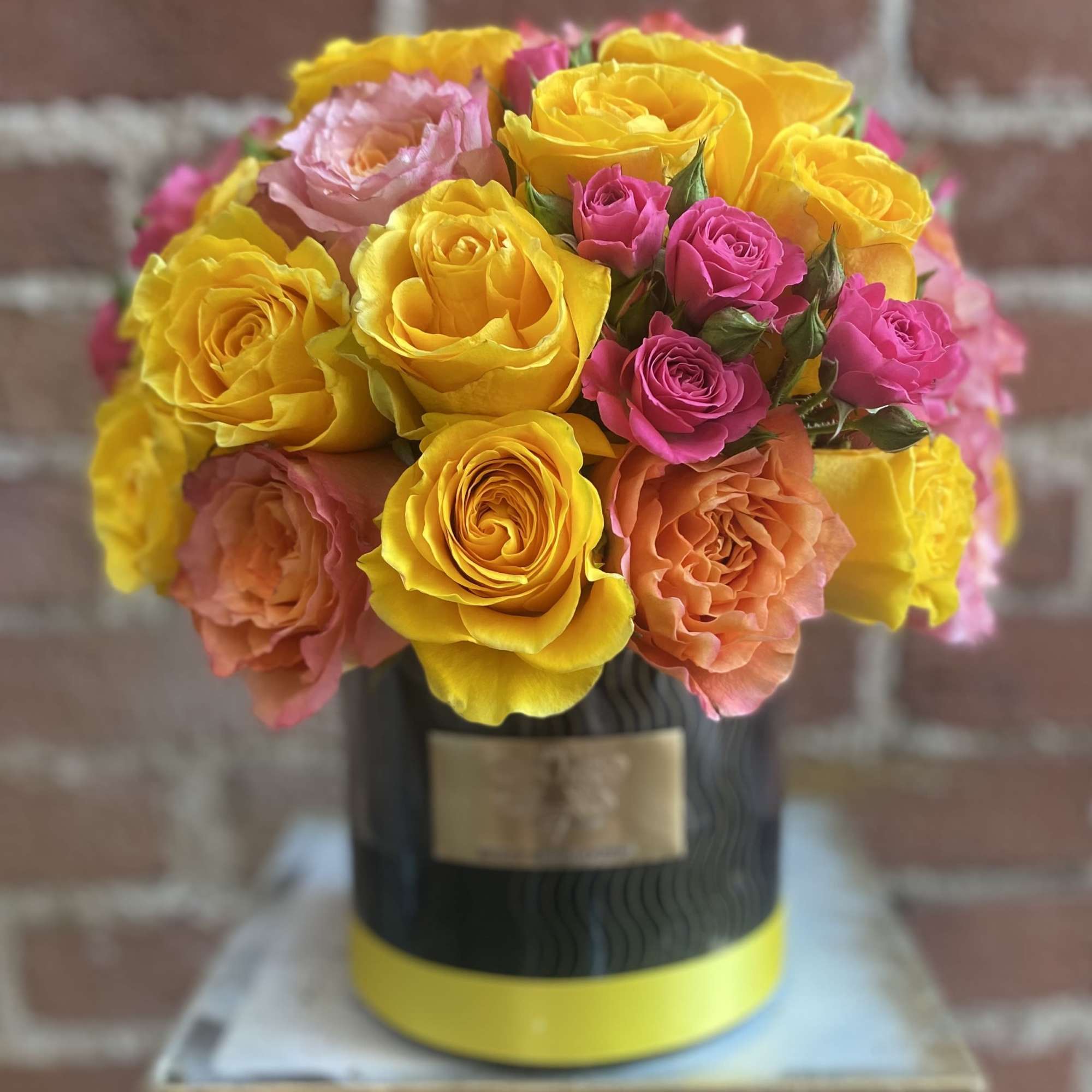 Bouquet of yellow, pink, and peach roses in a black hatbox