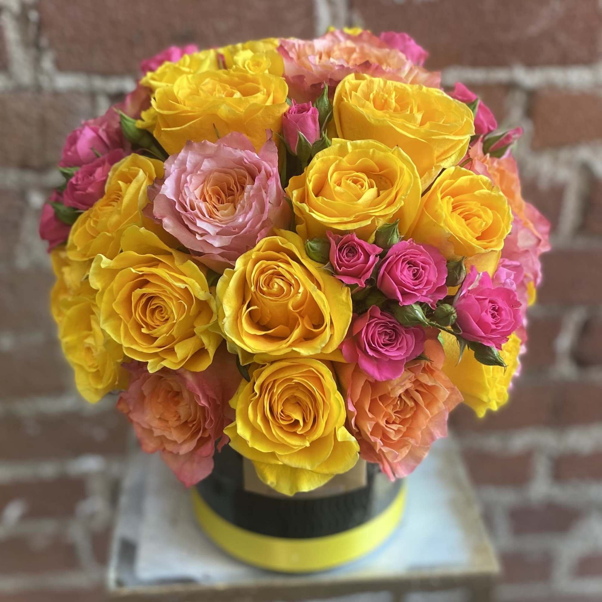 Bouquet of yellow, pink, and peach roses in a round box