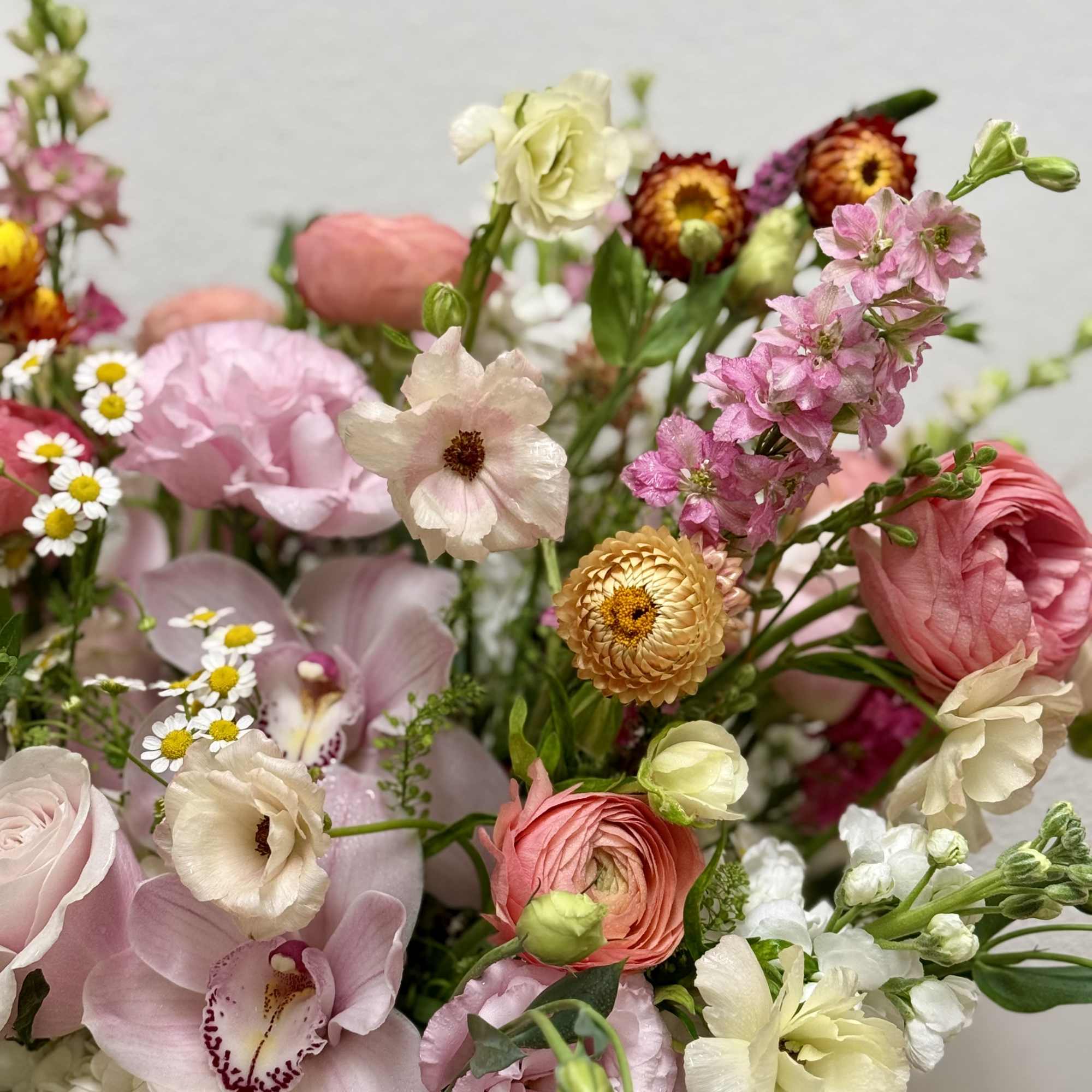 Pastel arrangement of roses, orchids, ranunculus, lisianthus, and mixed blooms in soft pink, peach, and cream.