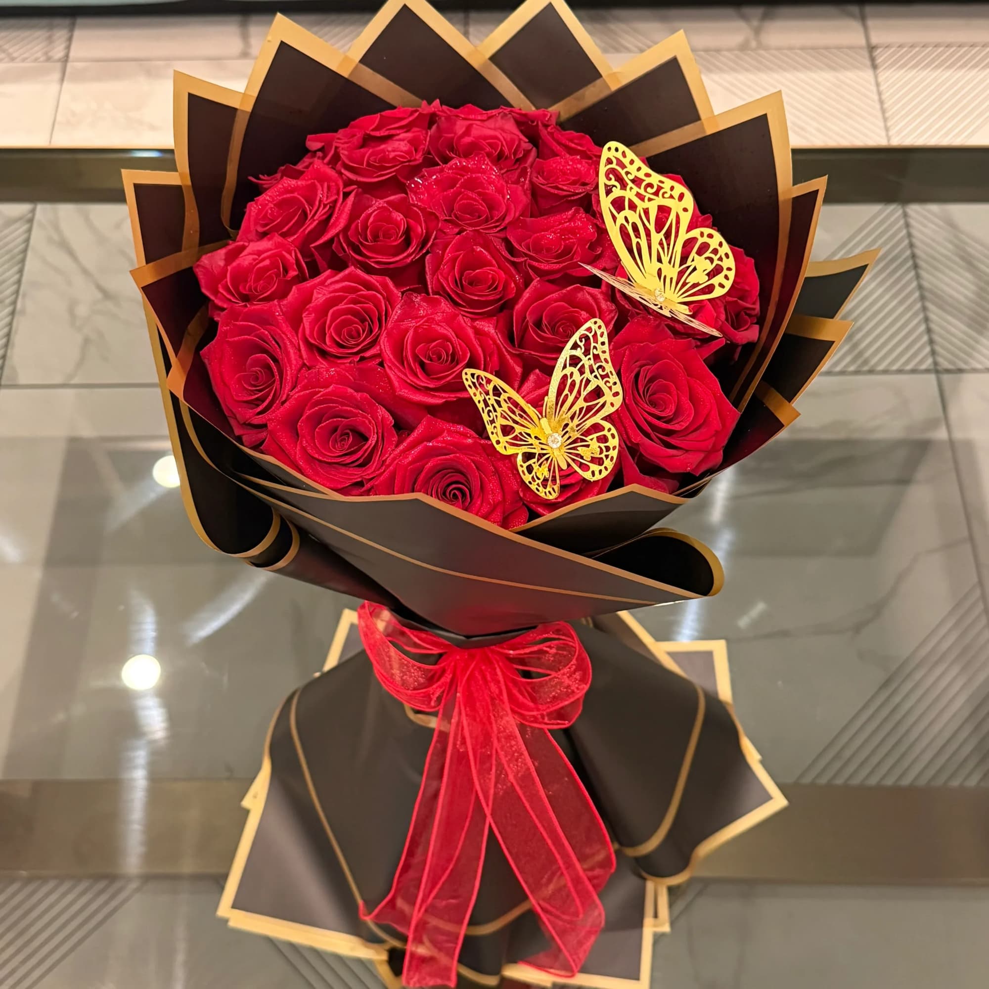Bouquet of red roses wrapped in black paper with gold trim and a red ribbon