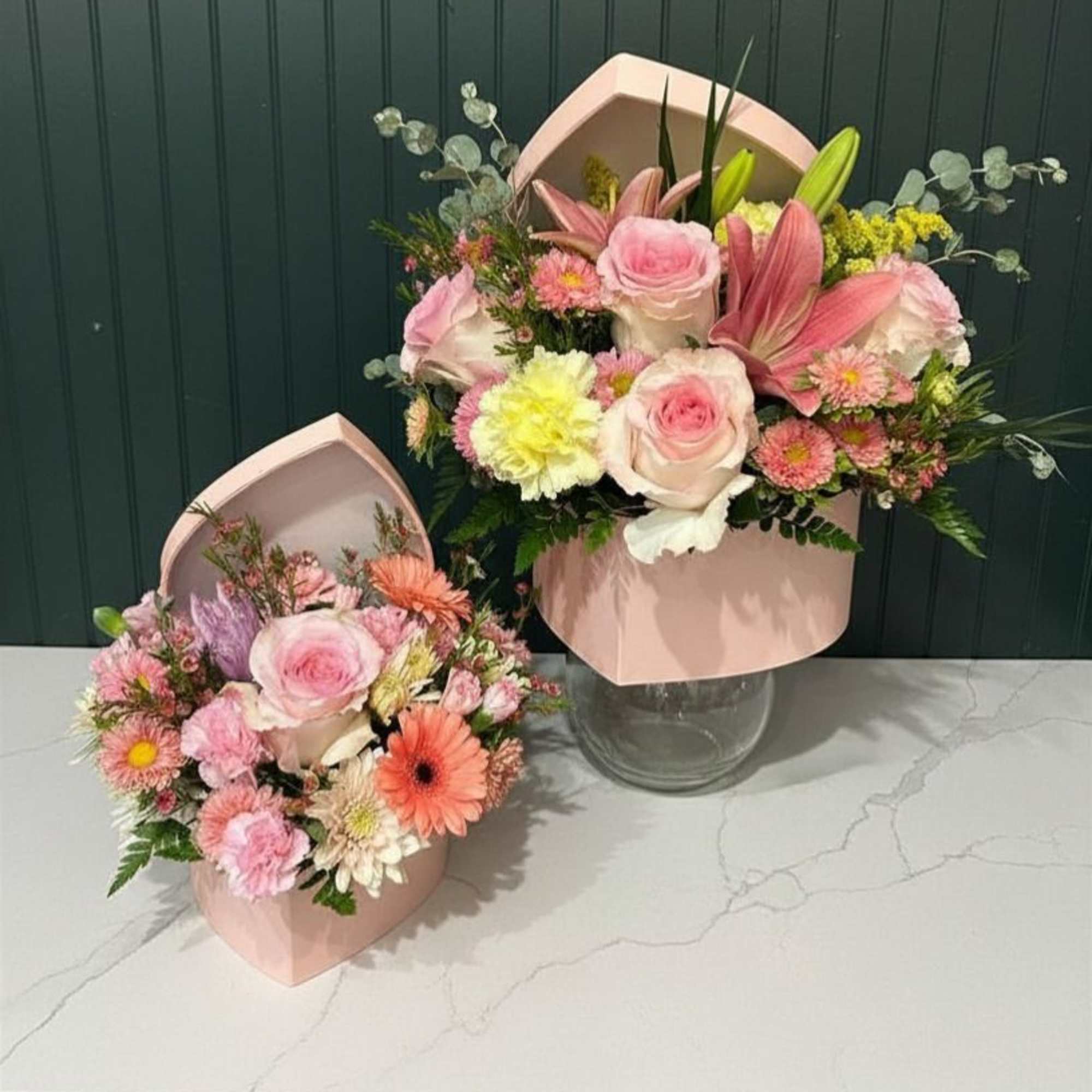 A blush pink hatbox filled with soft pink roses, pale lilies, and