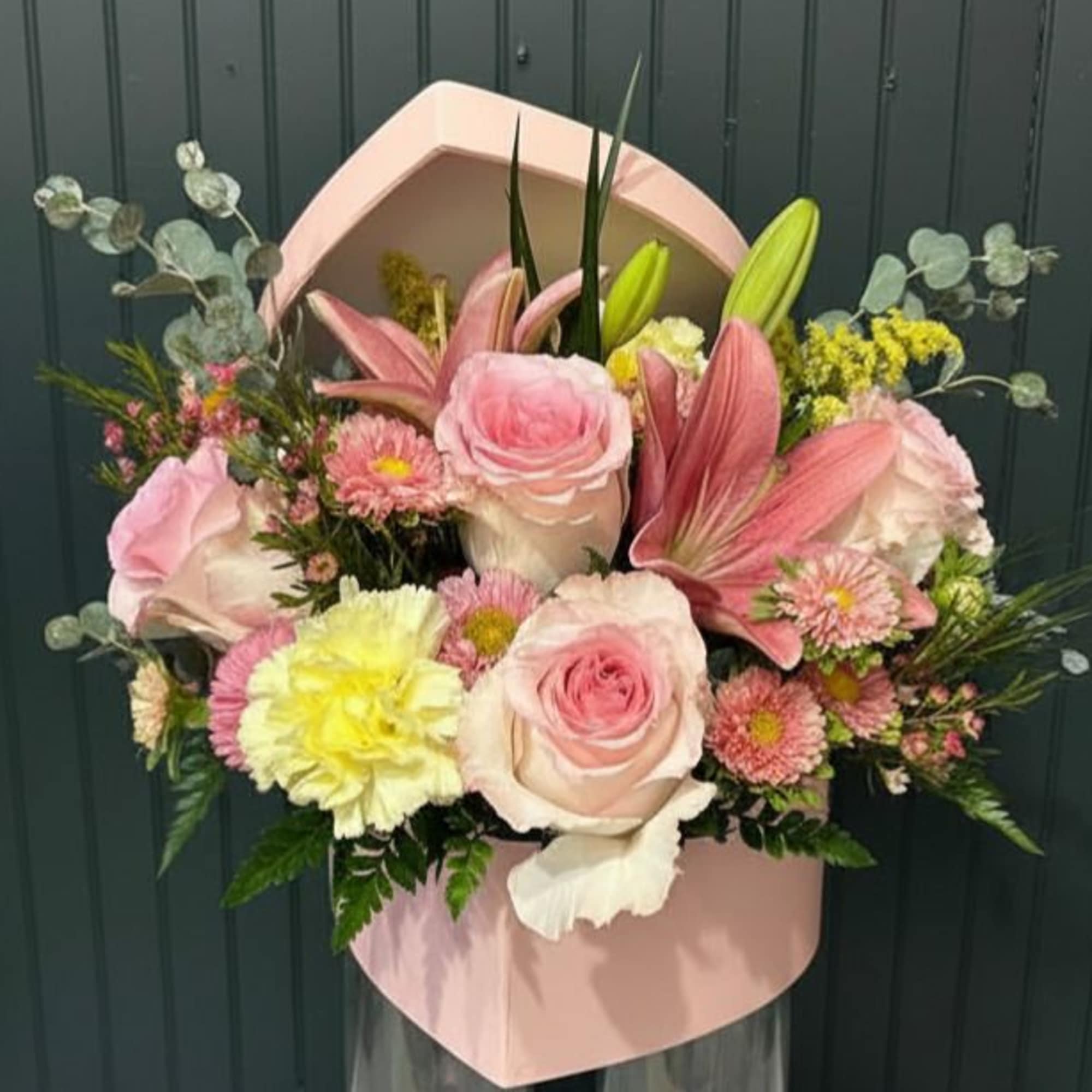 A blush pink hatbox filled with soft pink roses, pale lilies, and