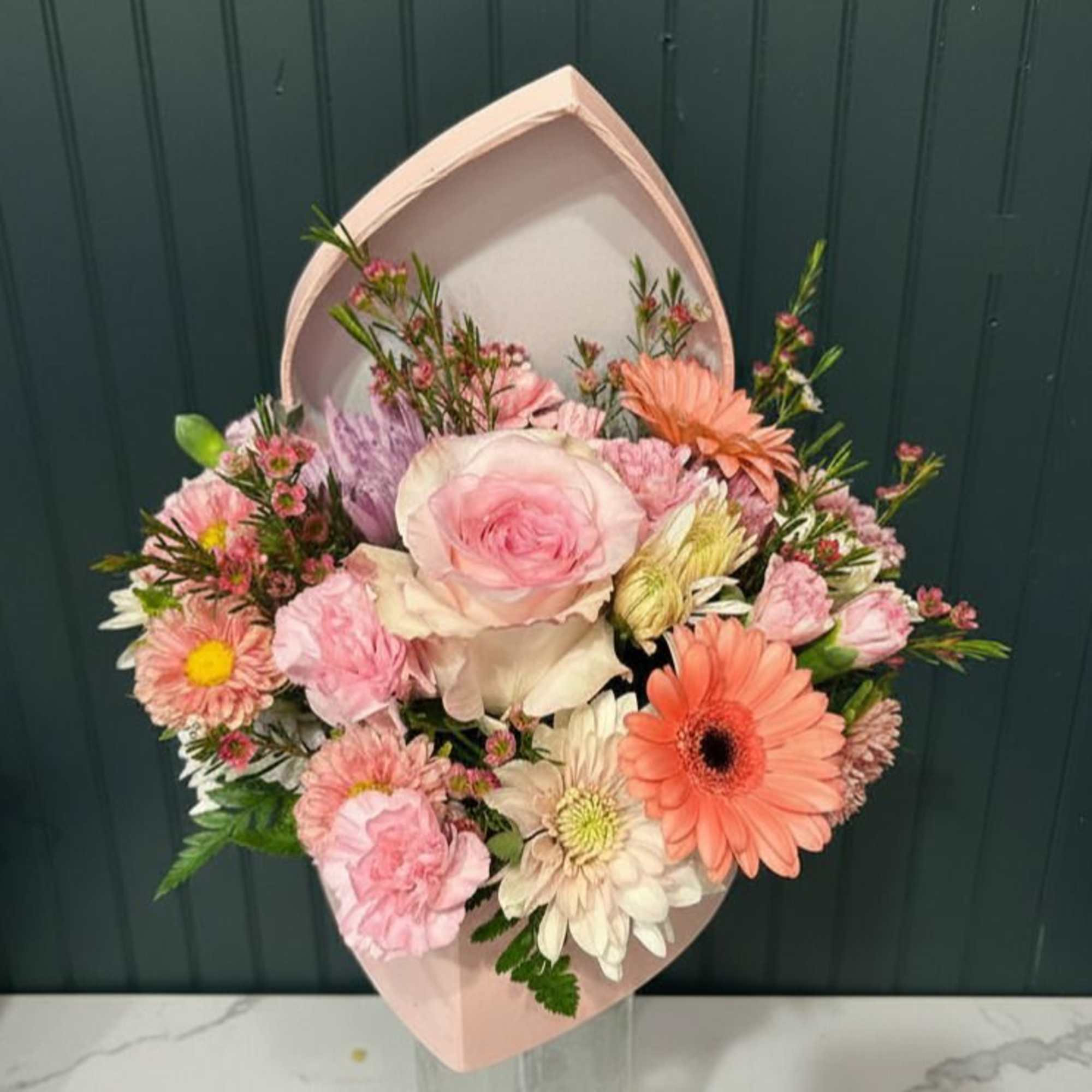A blush pink hatbox filled with soft pink roses, pale lilies, and