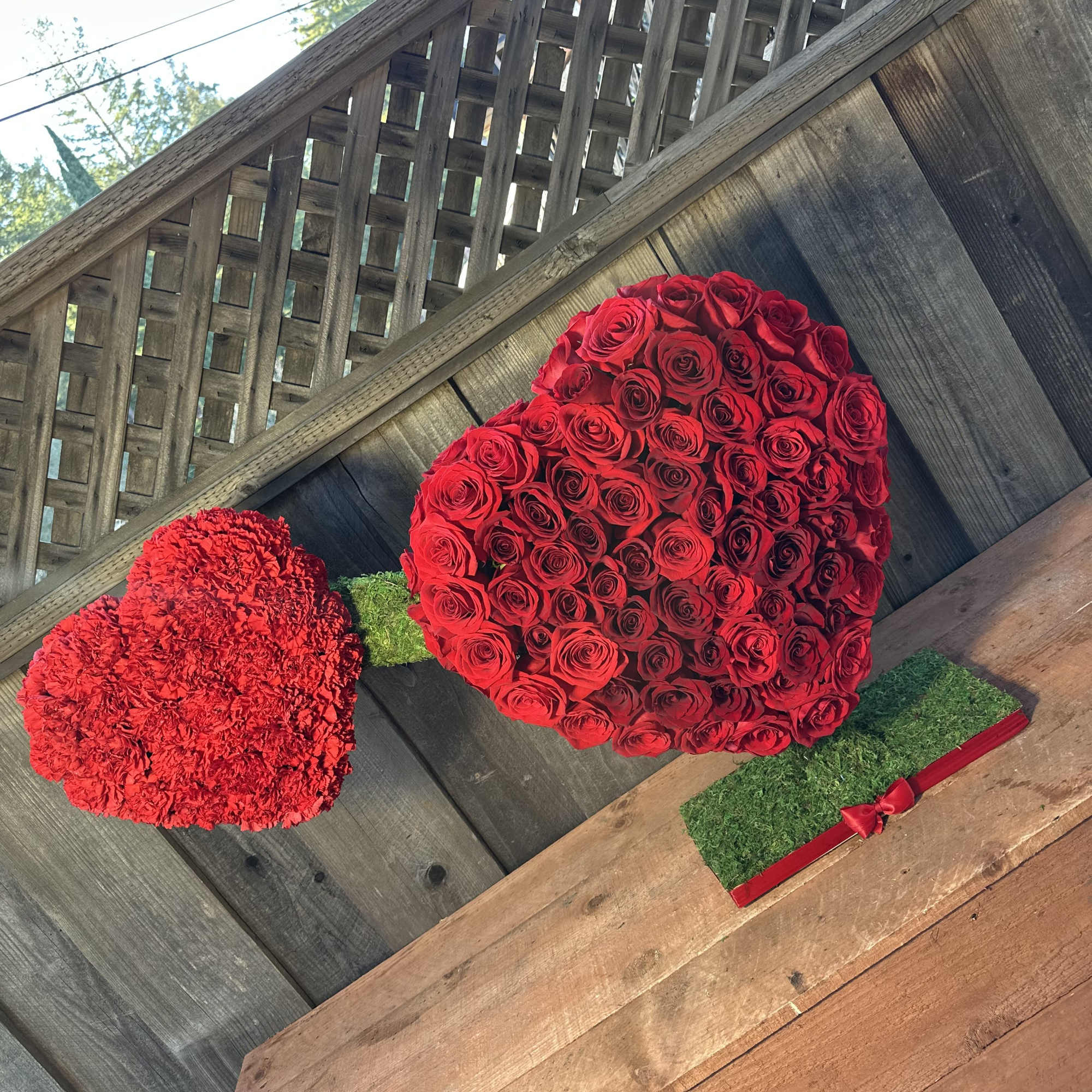 Heart-shaped red rose arrangement with a red carnation heart beside it