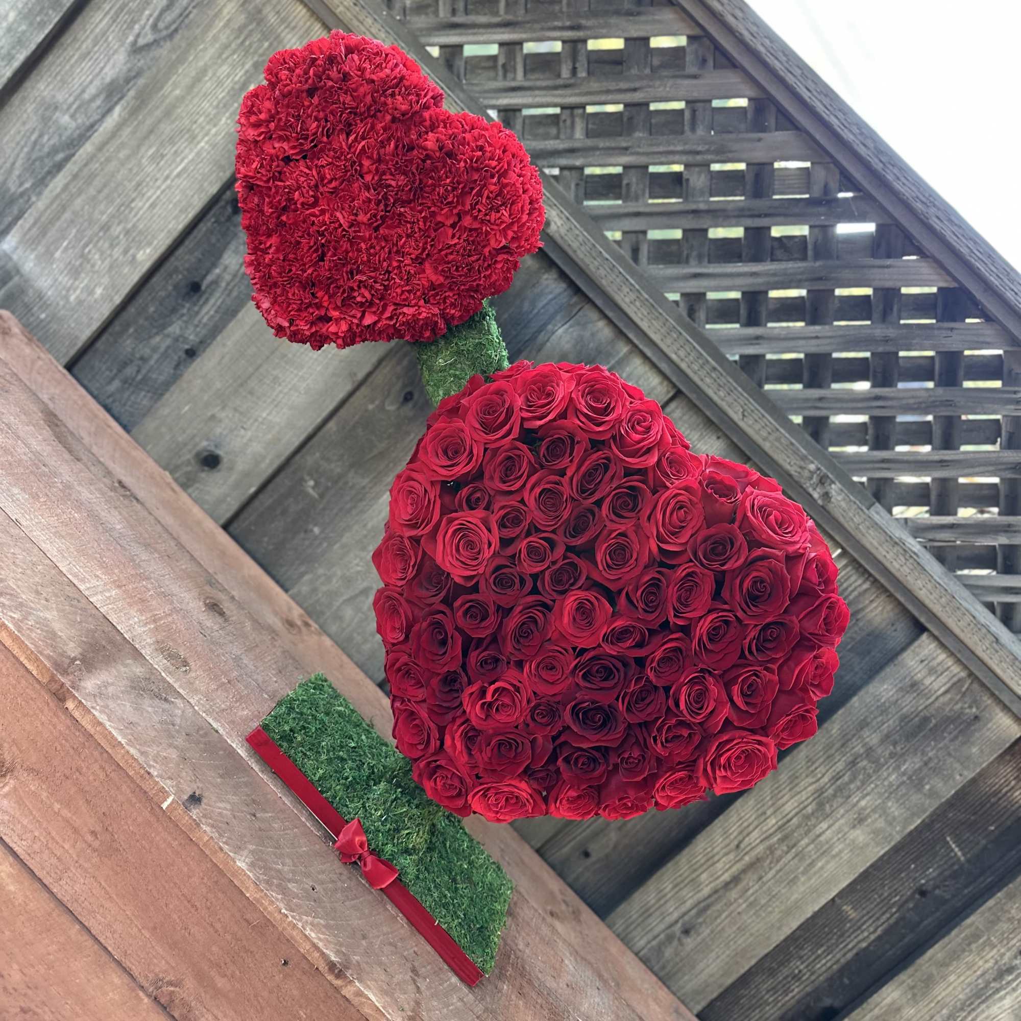 Two red heart-shaped floral arrangements on a wooden deck