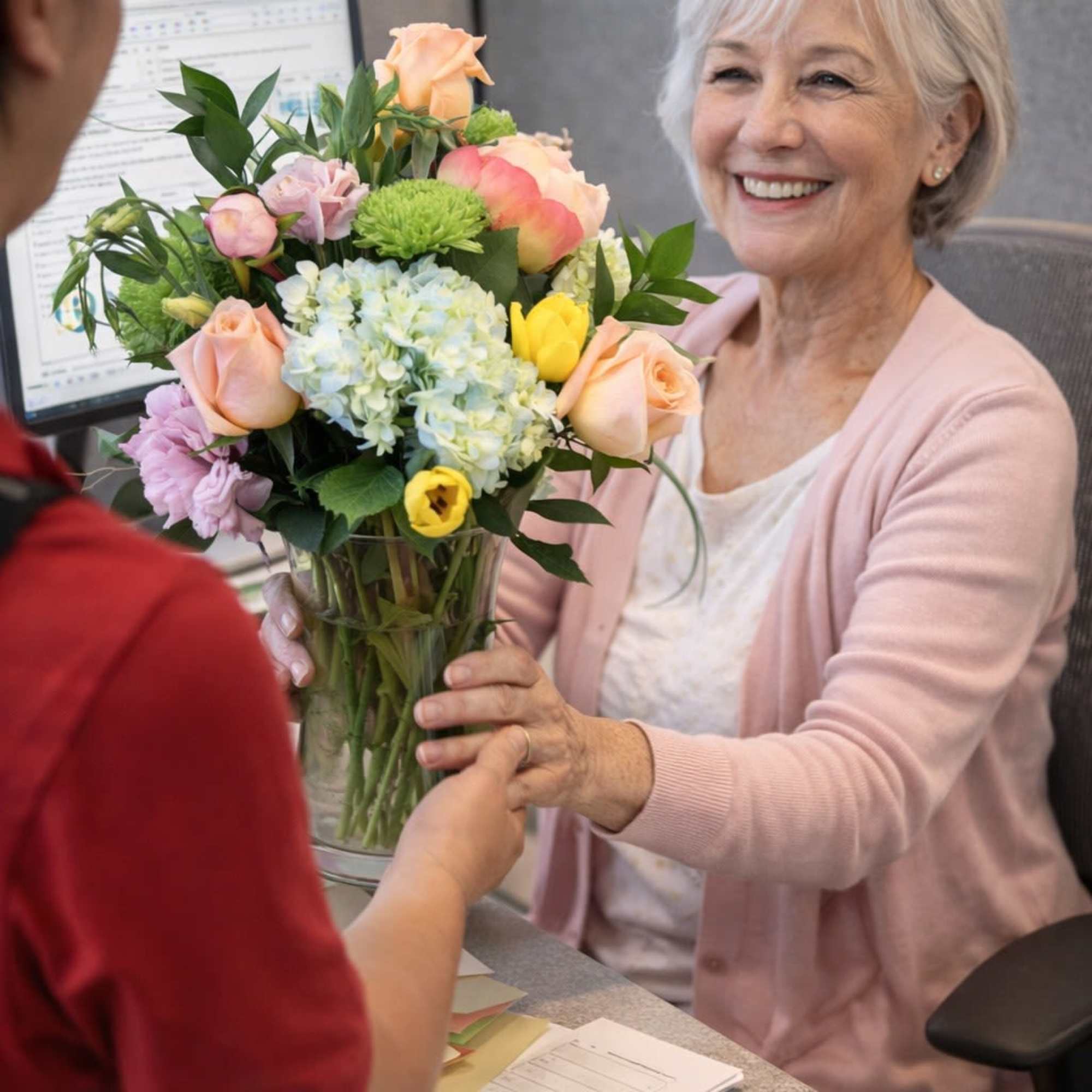 Woman receiving pastel bouquet of peach roses, yellow tulips, and blue hydrangea in a clear glass vase