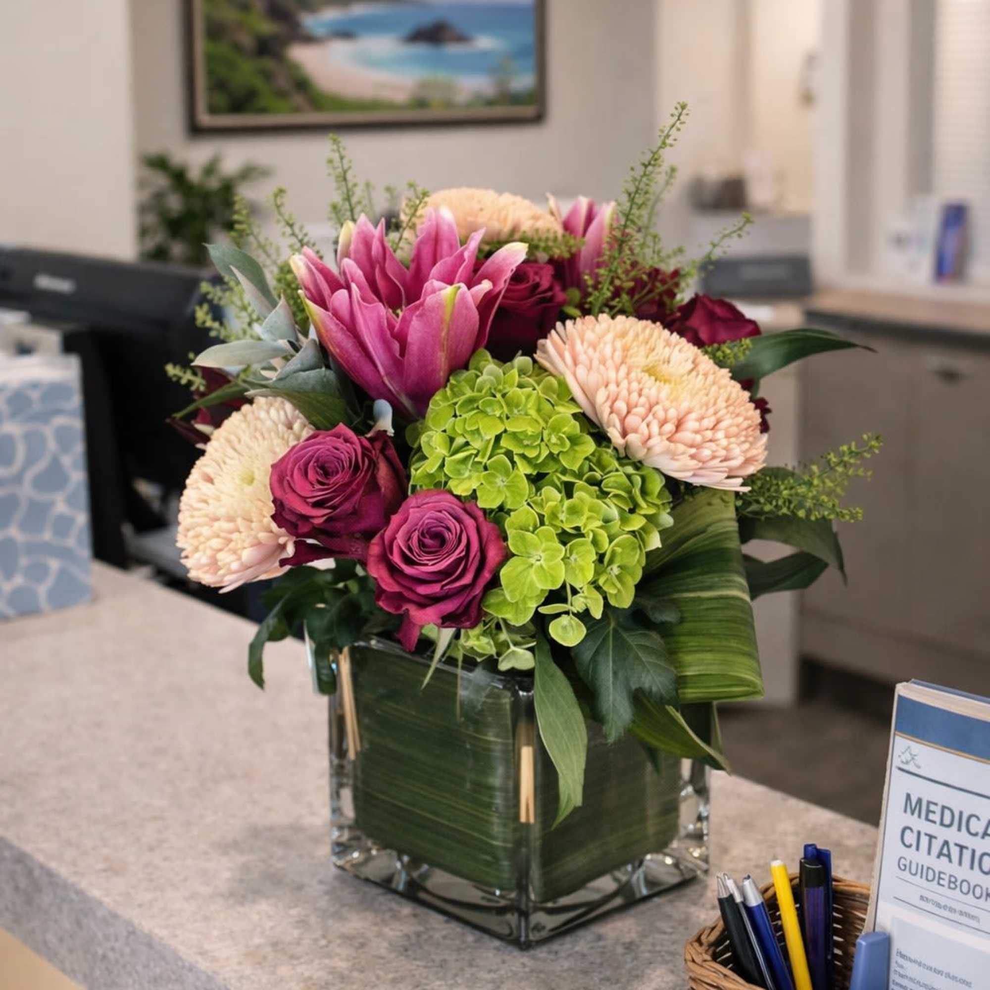 Vibrant arrangement of pink flowers, green hydrangea, and cream blooms in a glass cube vase on a countertop