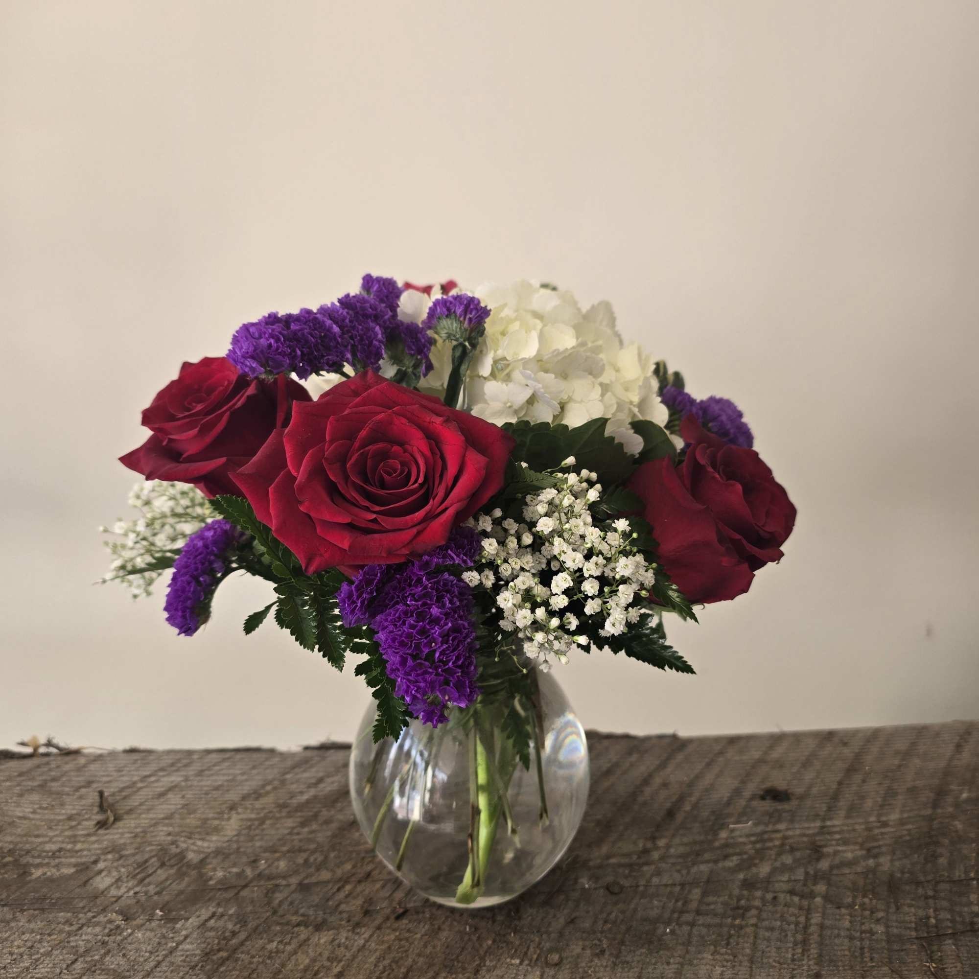 Bouquet of red roses, white hydrangea, and purple filler in a clear glass vase