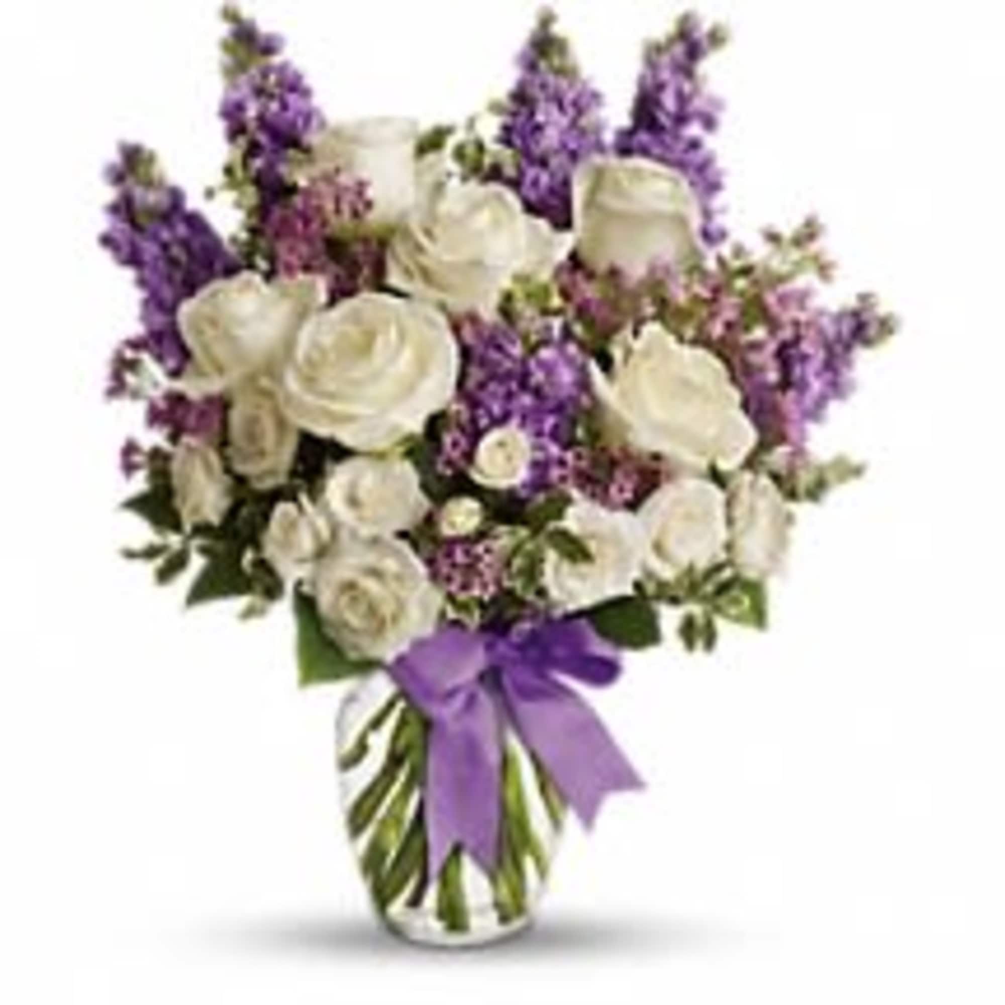Tall arrangement of white roses and purple flowers in a clear glass vase with a purple bow