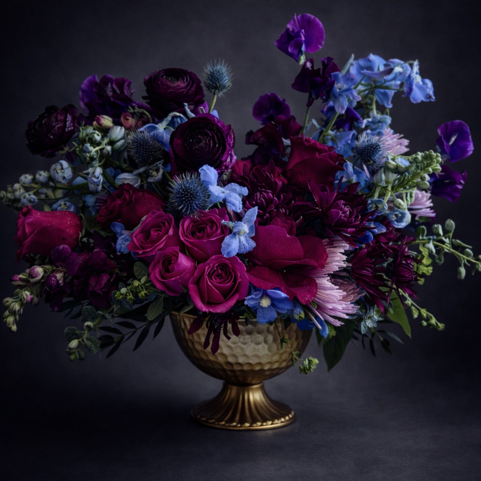 Purple and blue floral arrangement in a gold pedestal vase