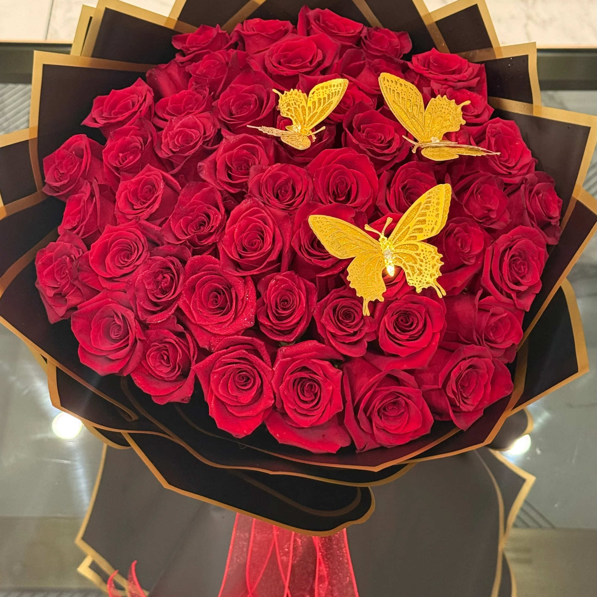 Bouquet of red roses with gold butterfly accents and black wrapping