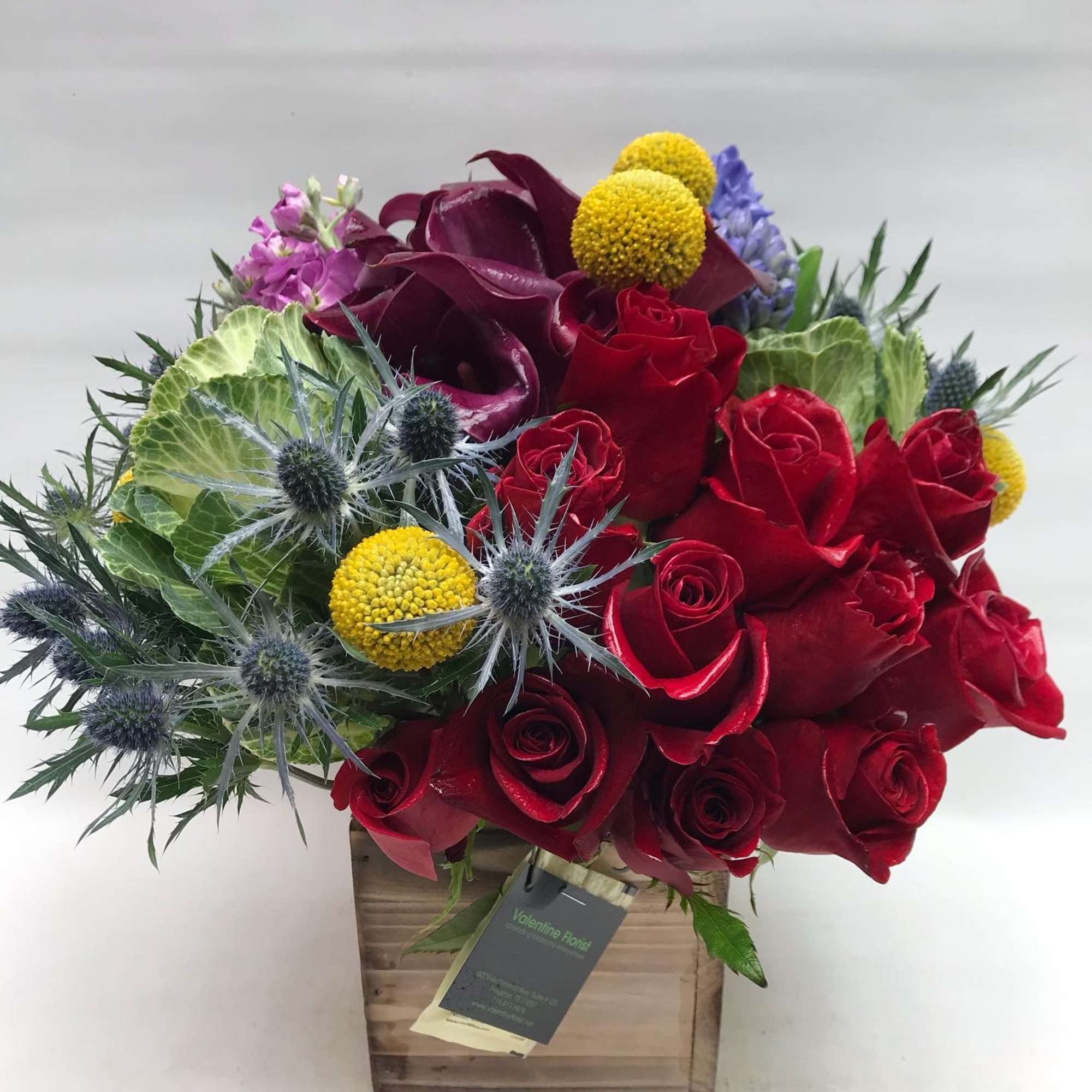 Bouquet of red roses with purple calla lilies and yellow pom-pom flowers in a wooden box
