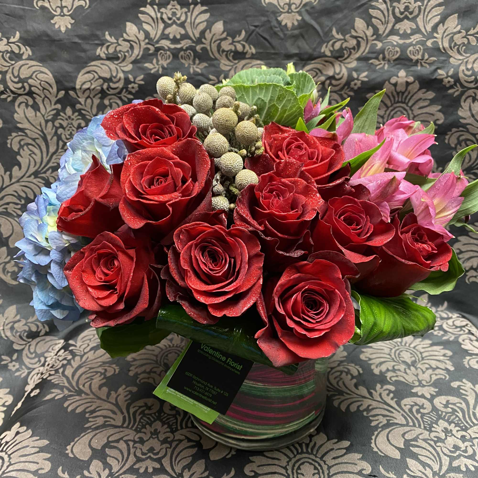 Red roses with blue hydrangea and pink lilies in a glass vase