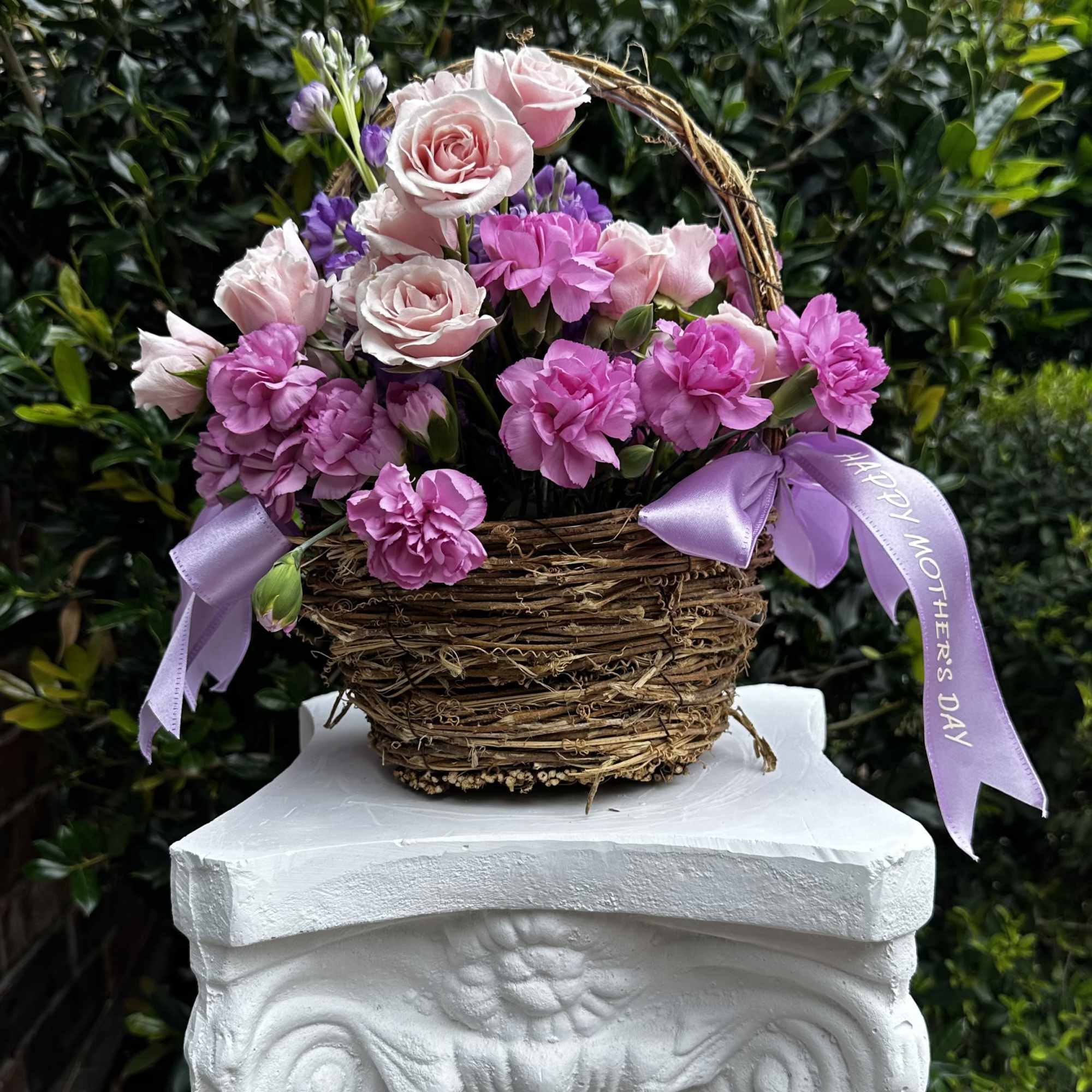 Pink roses and carnations in a wicker basket with lavender ribbons