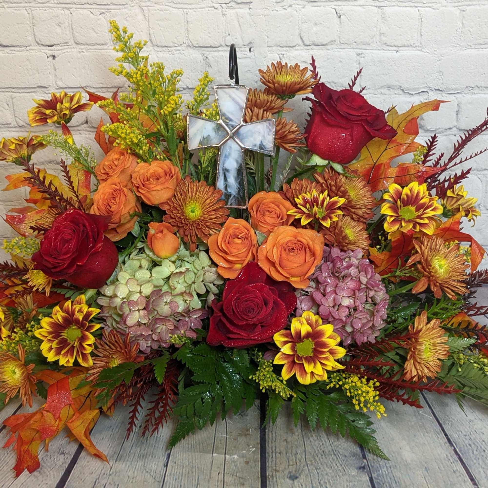 Autumn floral arrangement with red and orange roses, chrysanthemums, and a cross ornament