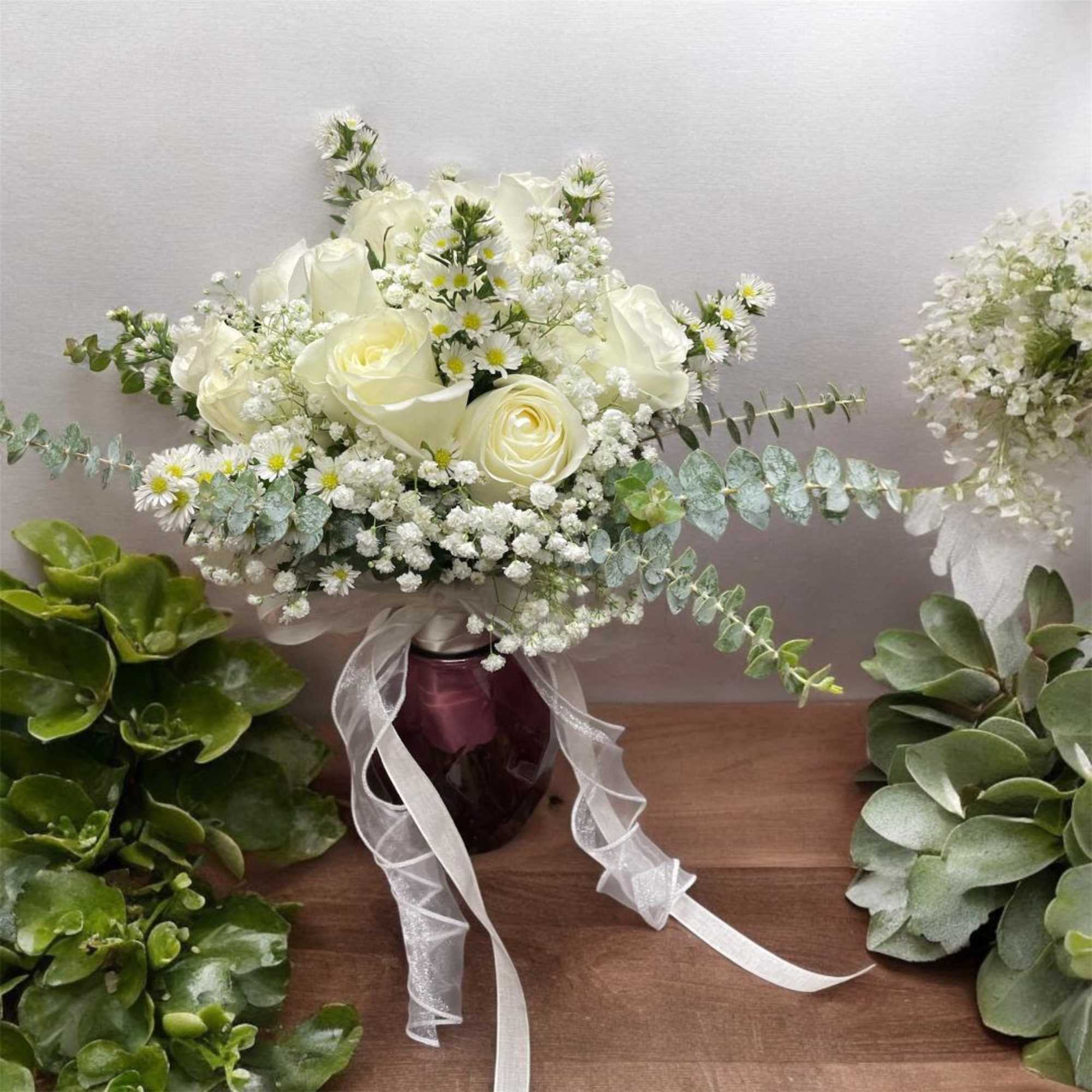 White rose bouquet with baby's breath in a dark vase and white ribbon