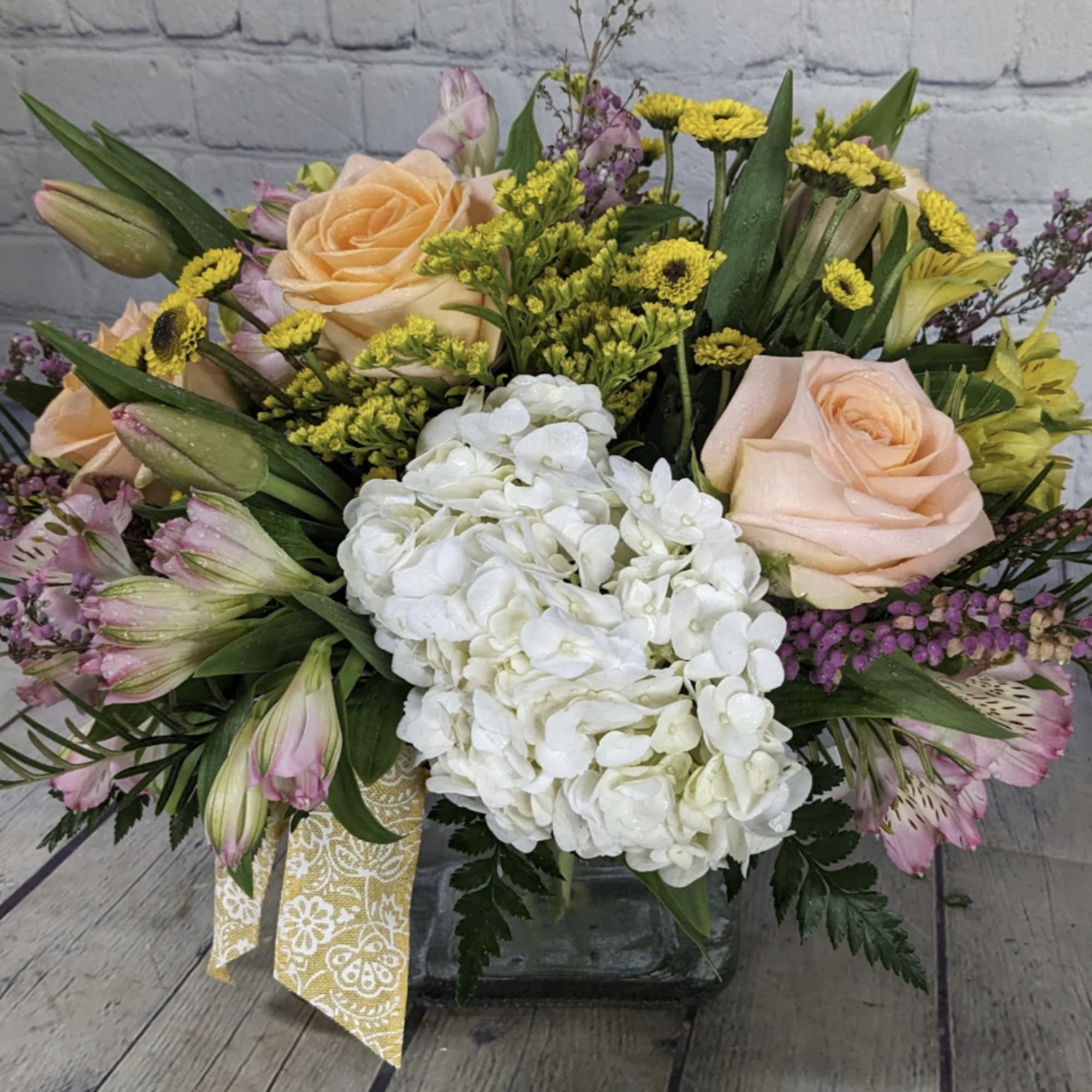 Mixed bouquet with peach roses, white hydrangea, and yellow accents in a glass vase