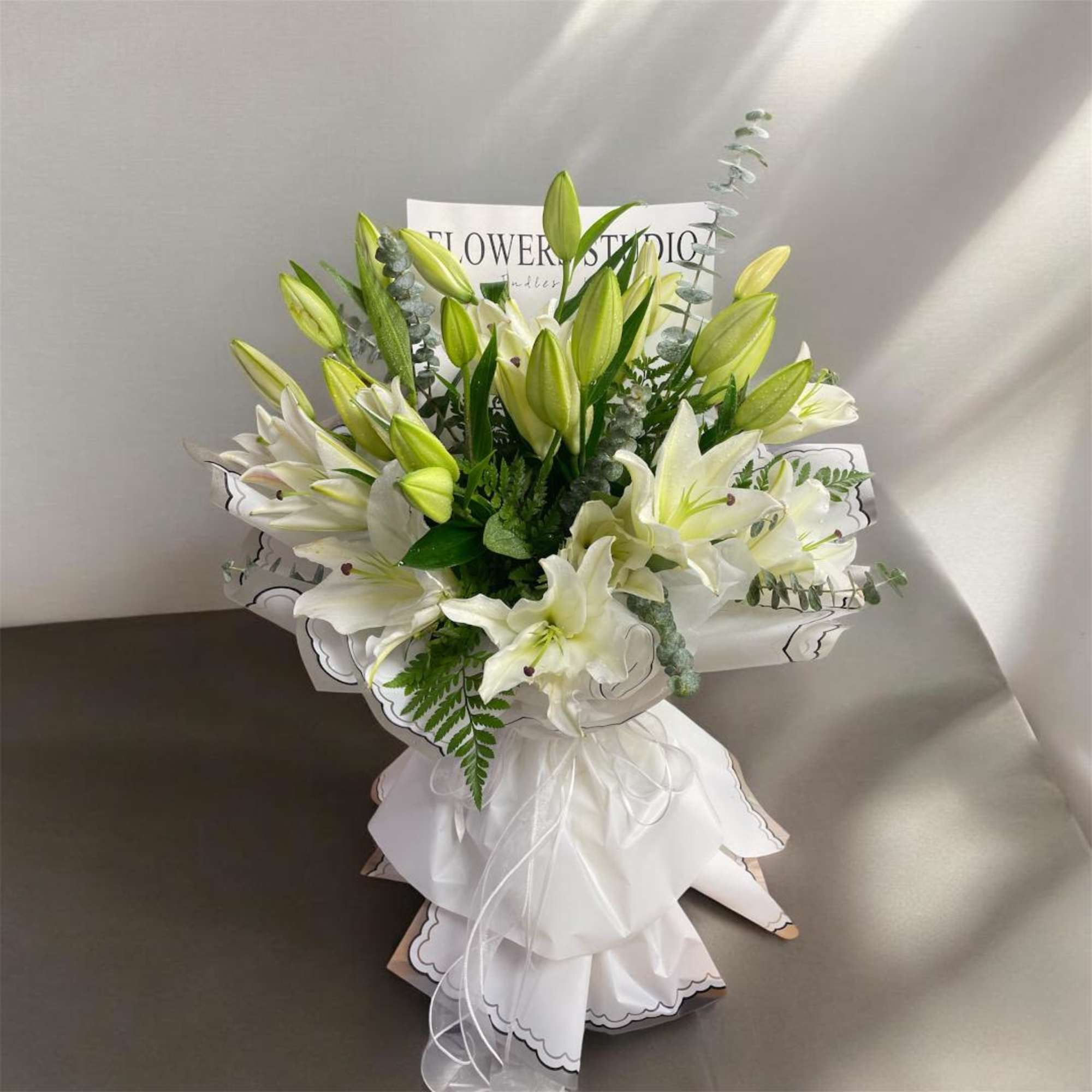 White lily bouquet with green buds and a white ribbon wrap