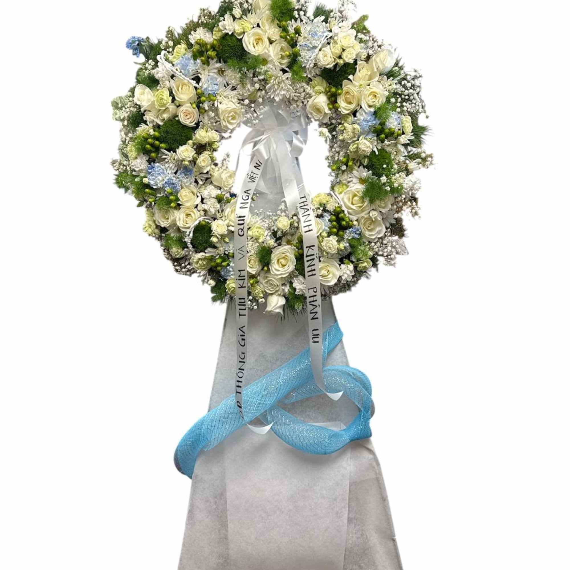 Large white floral wreath with blue ribbon on a gray stand