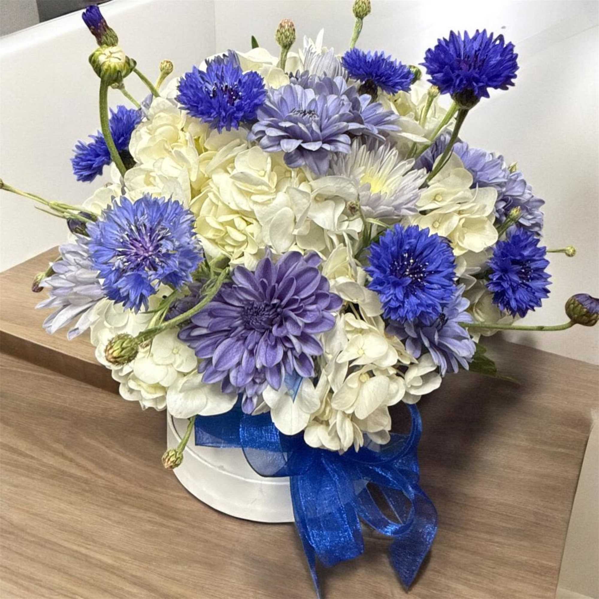 Blue and white mixed flower arrangement in a white hat box with ribbon