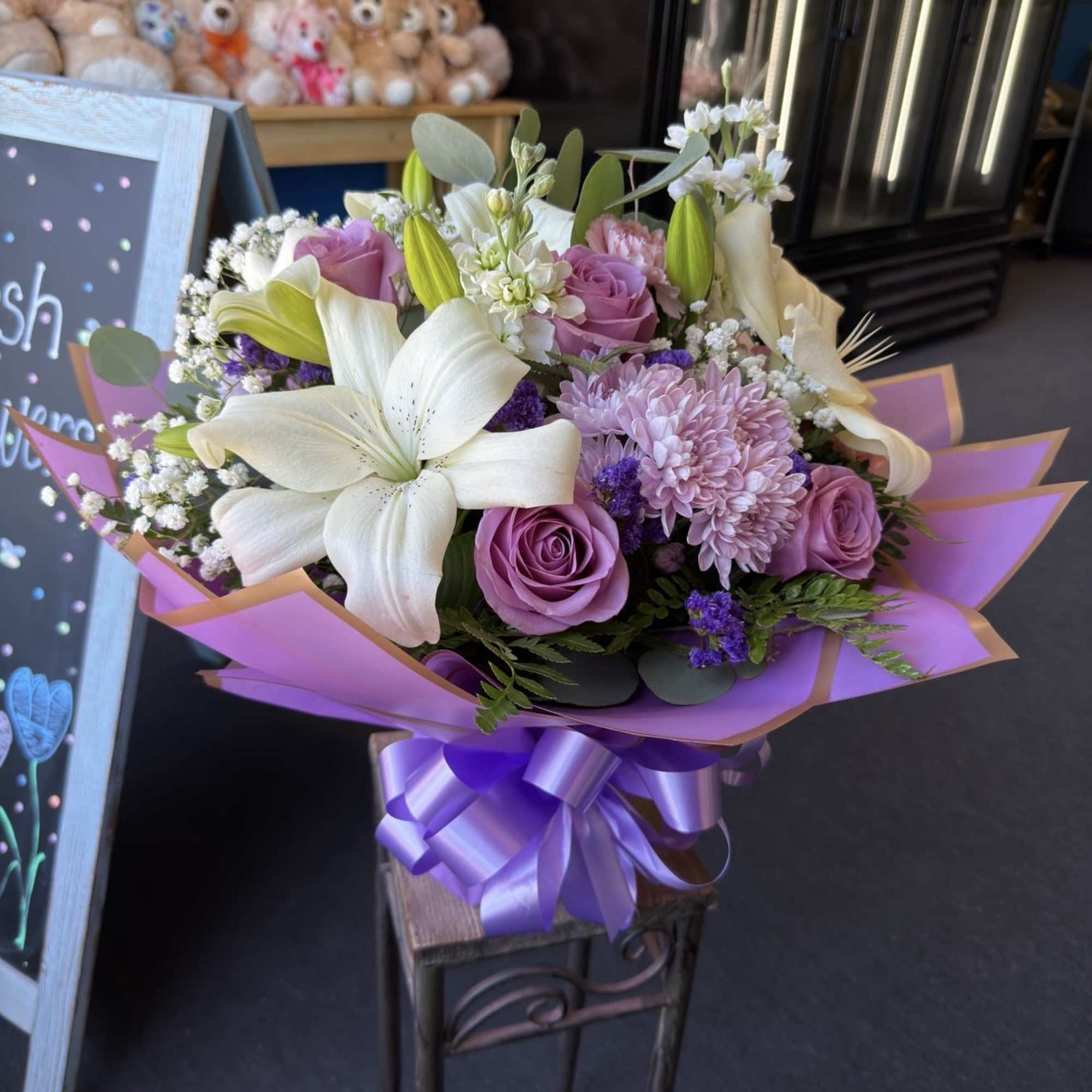 White lilies and lavender roses with pink chrysanthemums and greenery, wrapped in