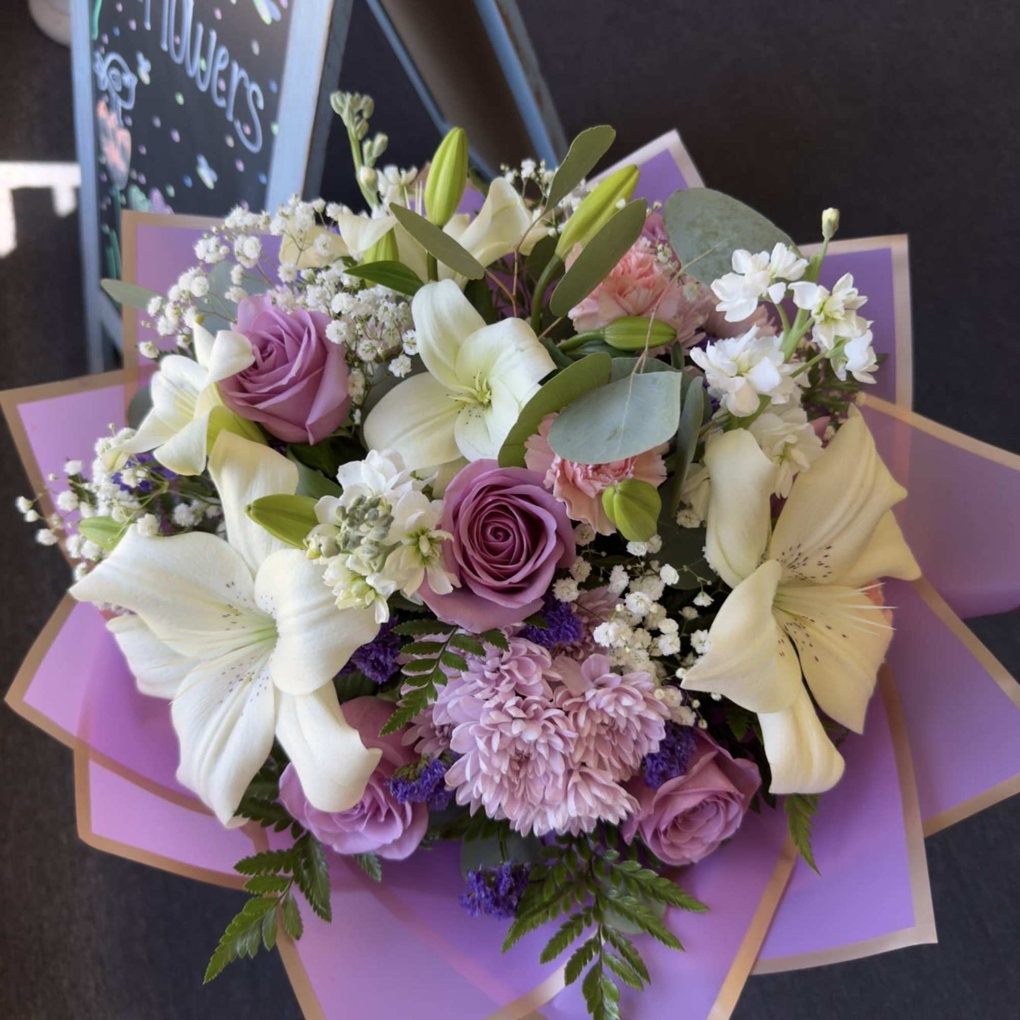 White lilies and lavender roses with pink chrysanthemums and greenery, wrapped in