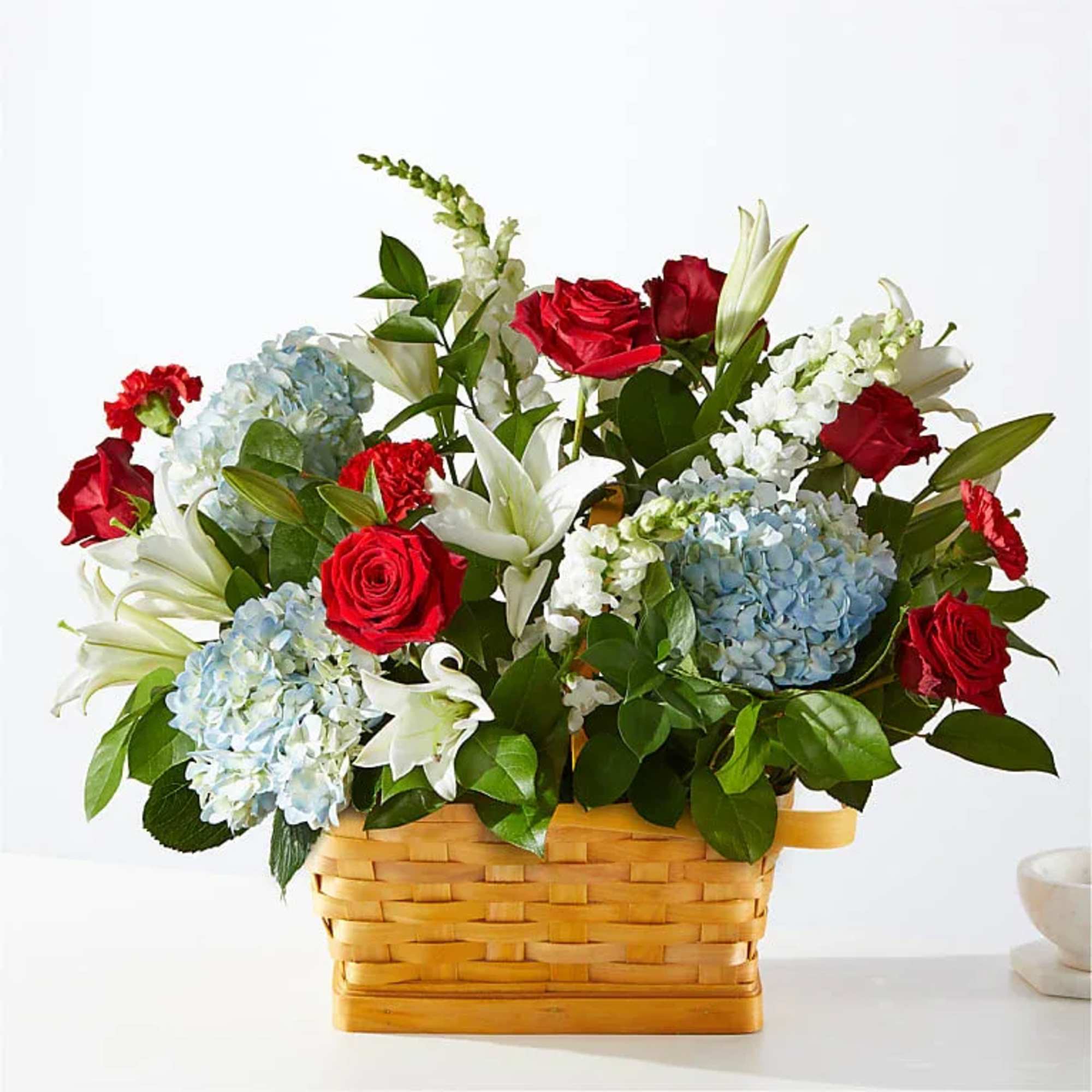 Basket arrangement of red roses, blue hydrangeas, and white lilies