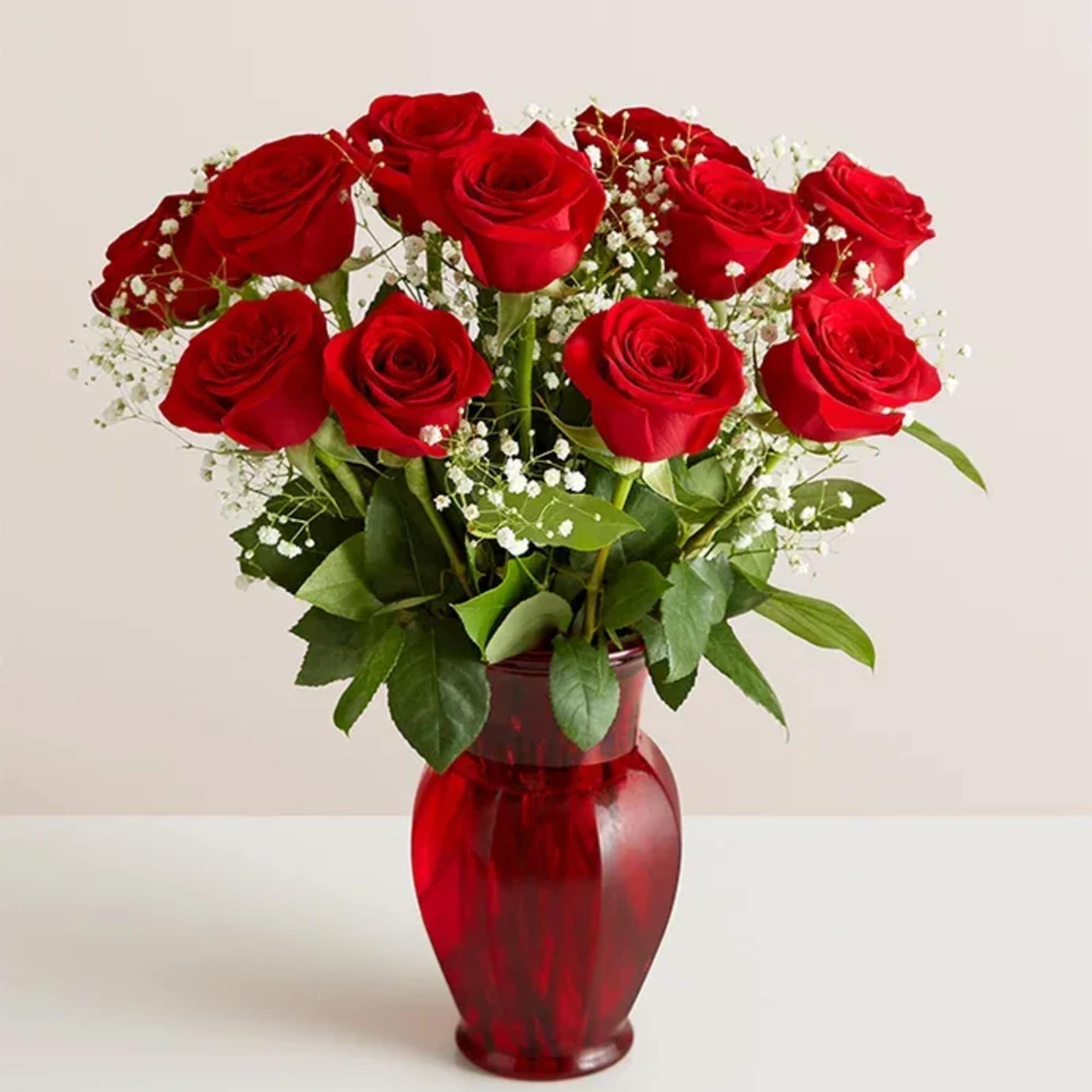 Red roses arranged in a red glass vase with baby's breath