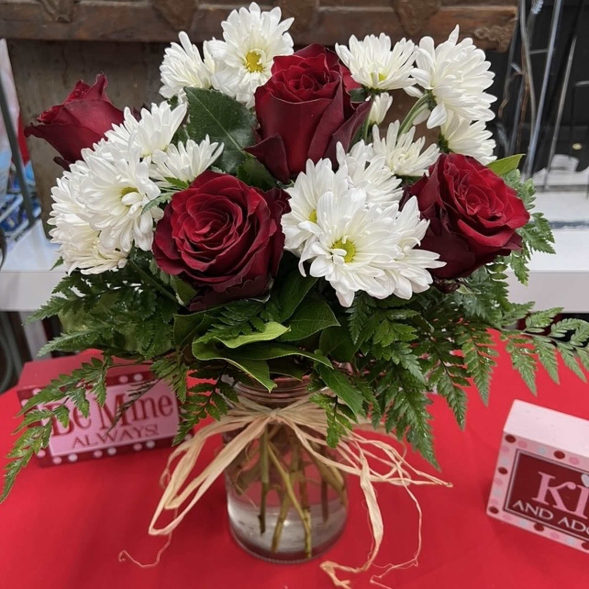 Red roses and white daisies in a glass vase with a raffia bow