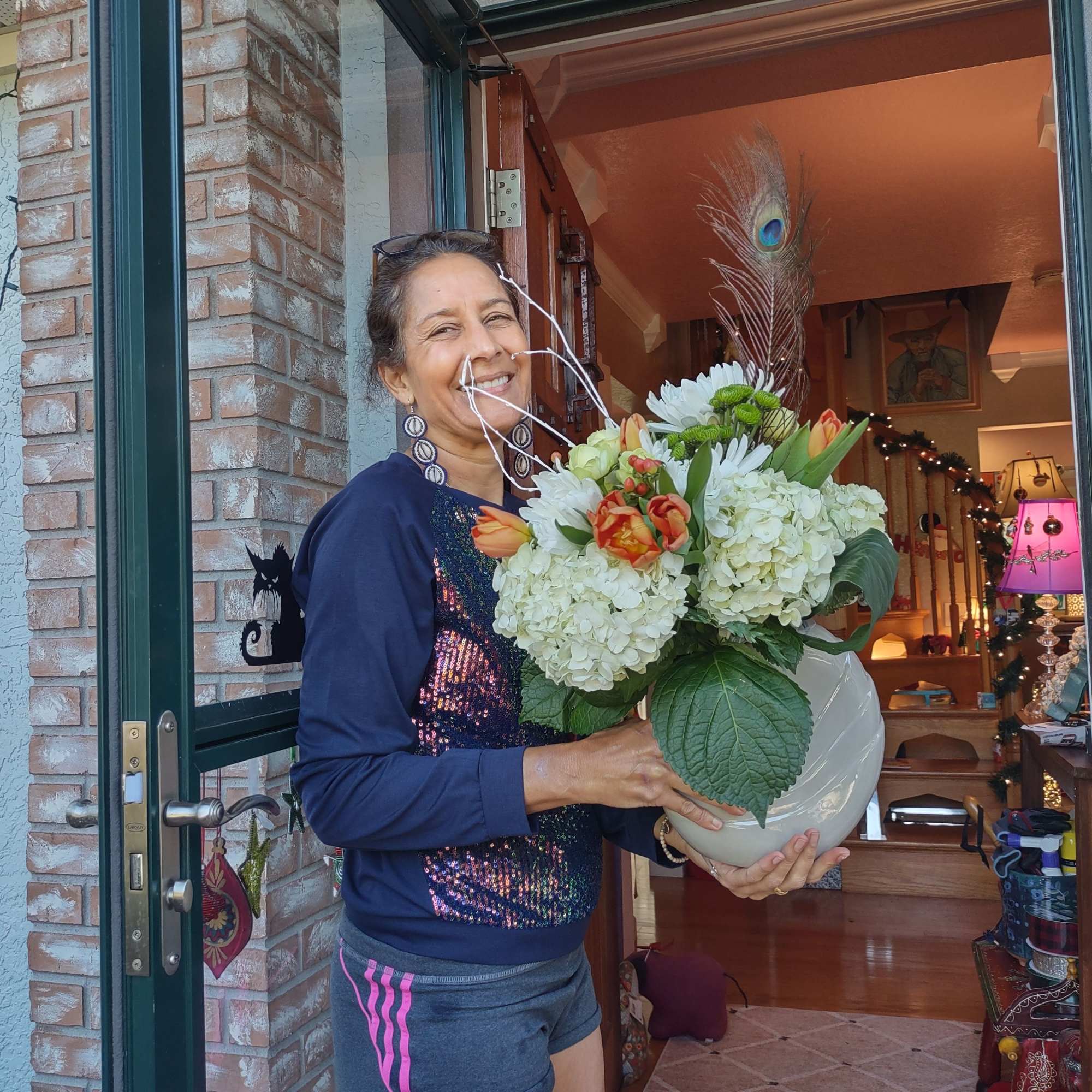 Woman holding a large white vase of mixed flowers at a doorway