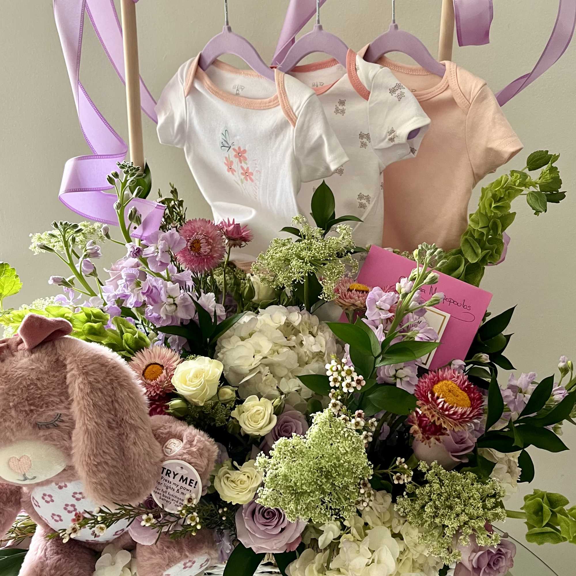 Gift basket with baby onesies, a plush bunny, and pastel flowers