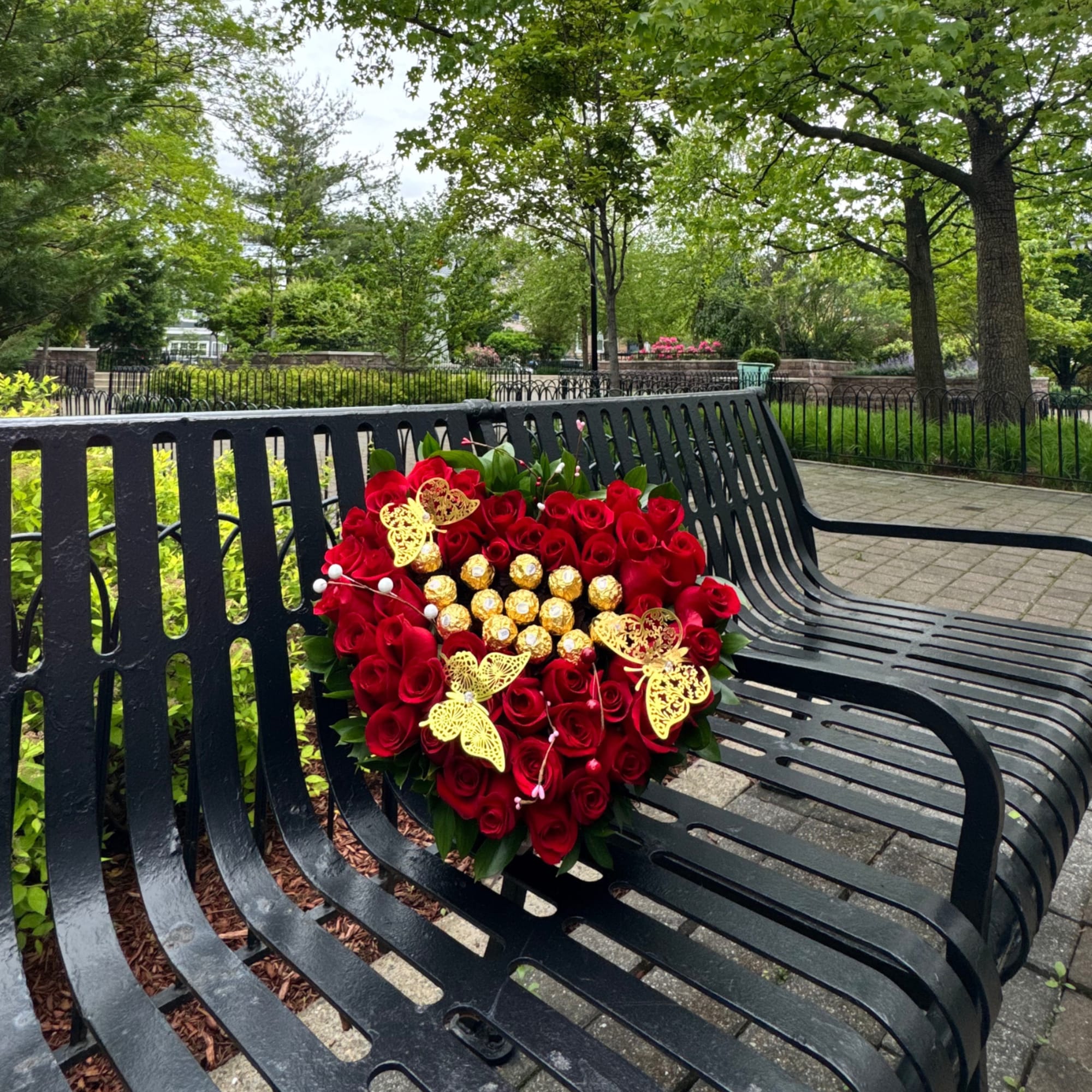 Heart-shaped bouquet of red roses with gold chocolates on a park bench
