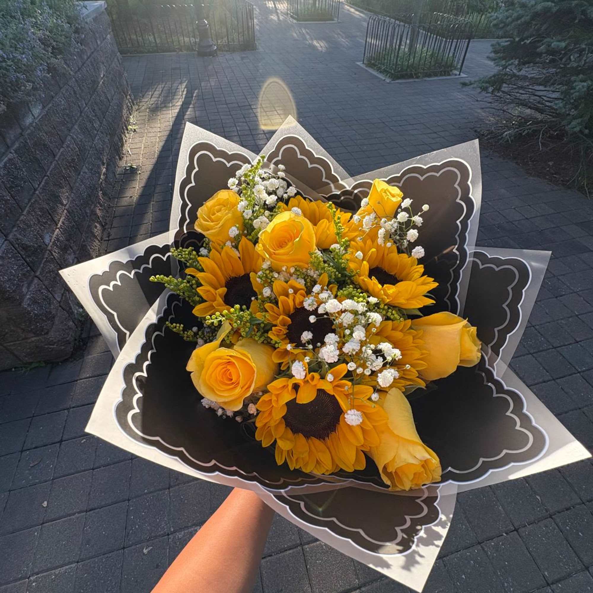 Handheld bouquet of yellow roses and sunflowers with white filler flowers