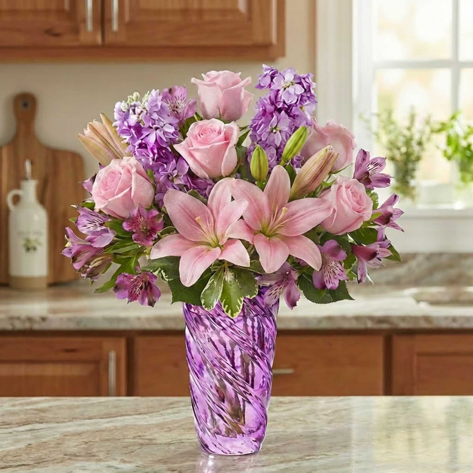 Pink roses and lilies arranged in a purple glass vase