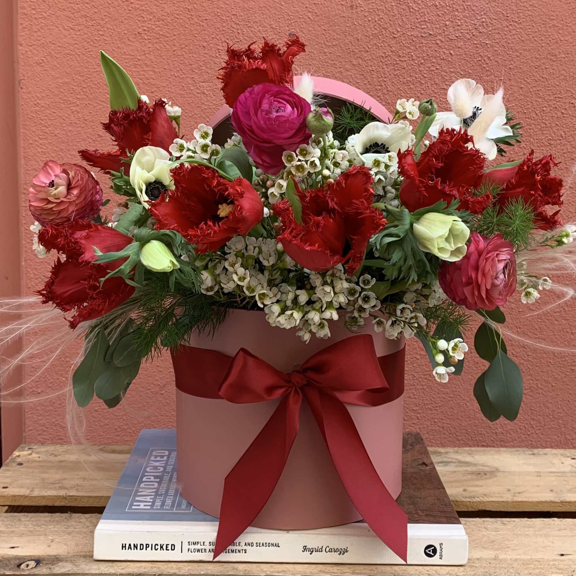Pink hatbox arrangement with red and white flowers and a red ribbon
