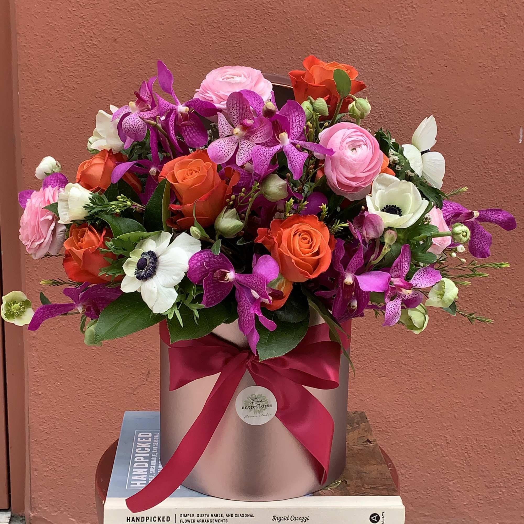 Mixed bouquet of pink, orange, purple, and white flowers in a round box with a ribbon.