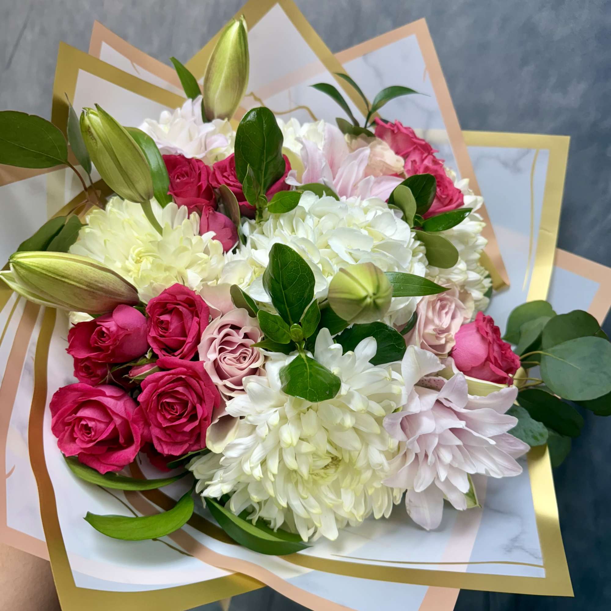 Bouquet of pink roses, white chrysanthemums, and lilies wrapped in pastel paper