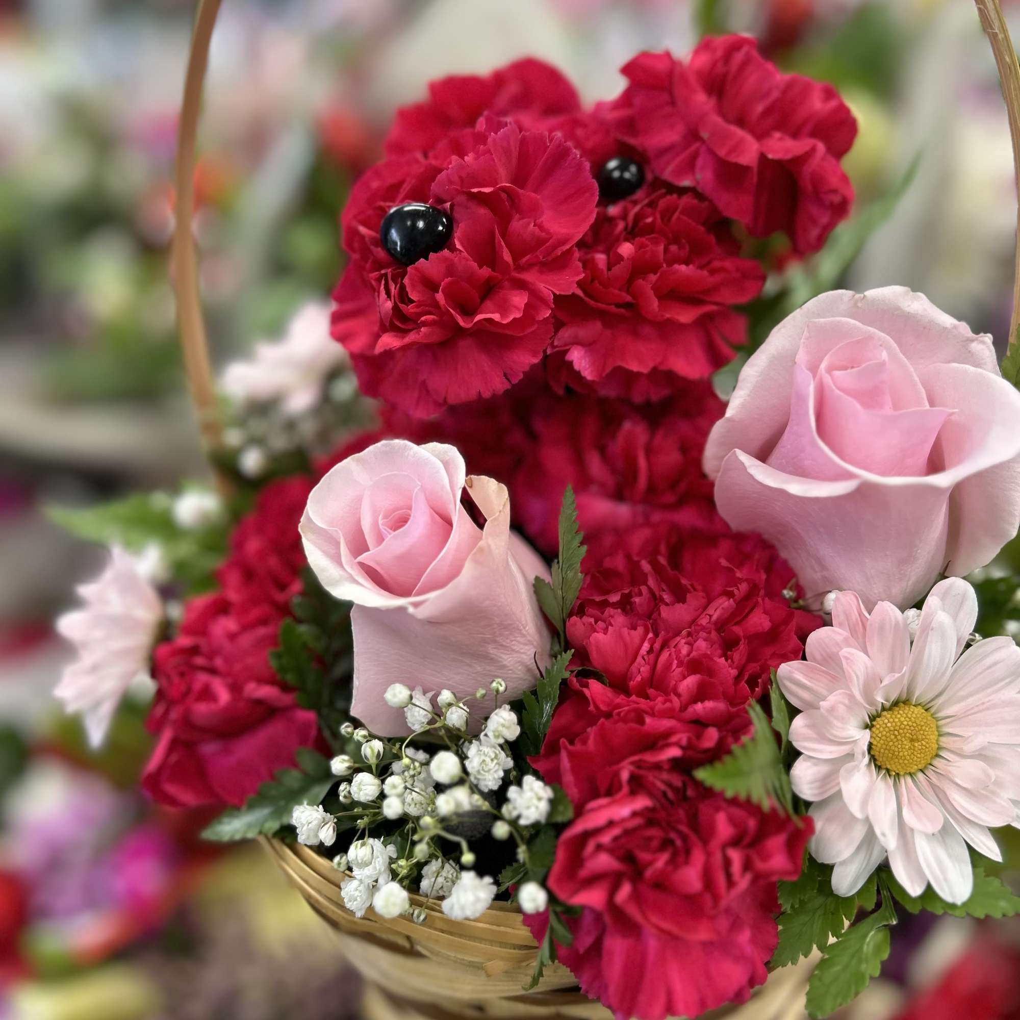 Basket arrangement with pink roses, red carnations, and a daisy
