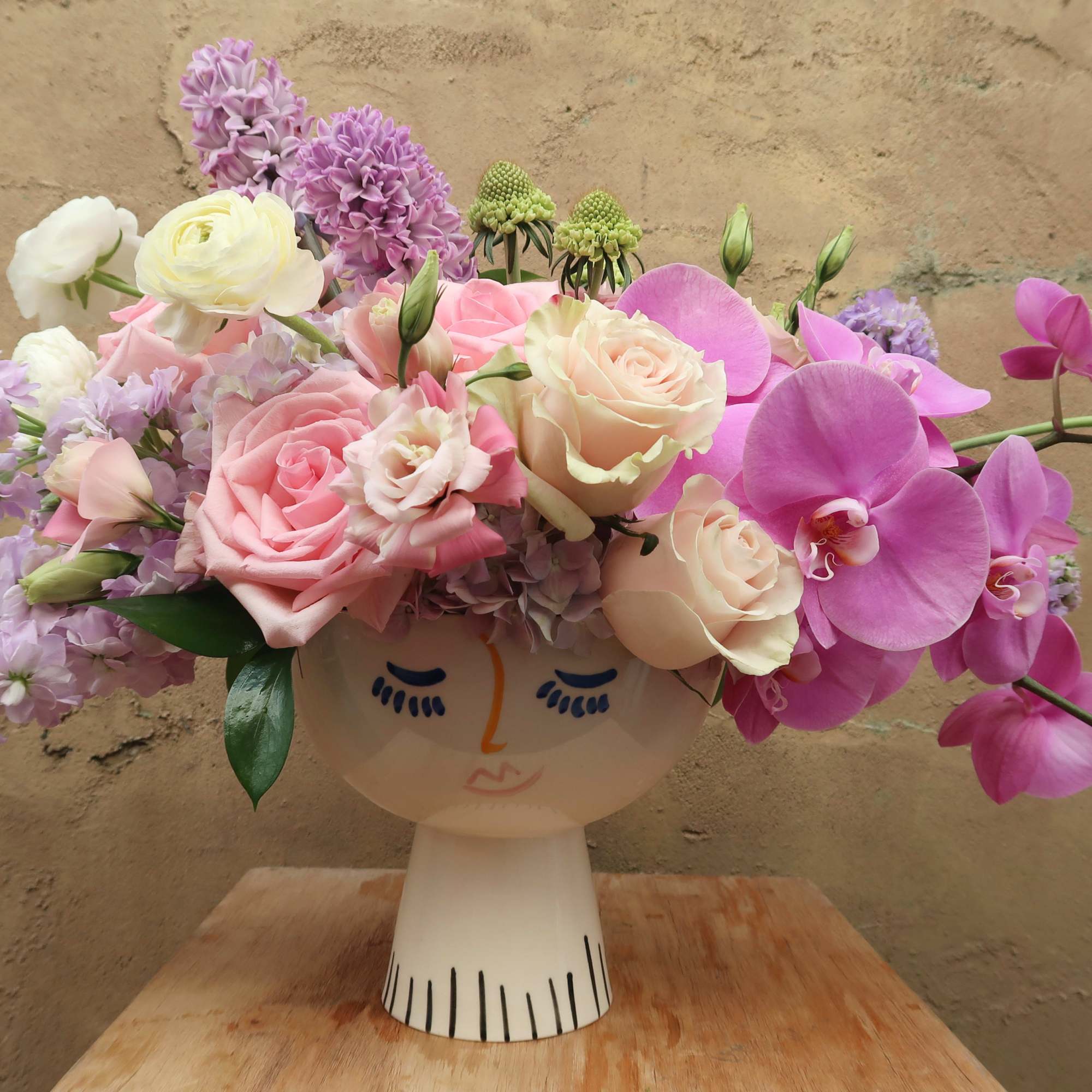 Pink and lavender flowers arranged in a face-shaped vase