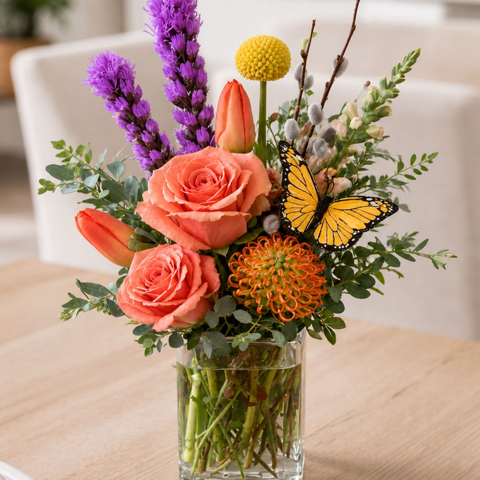 A lush, garden-style flower arrangement featuring roses, tulips, seasonal blooms, and decorative