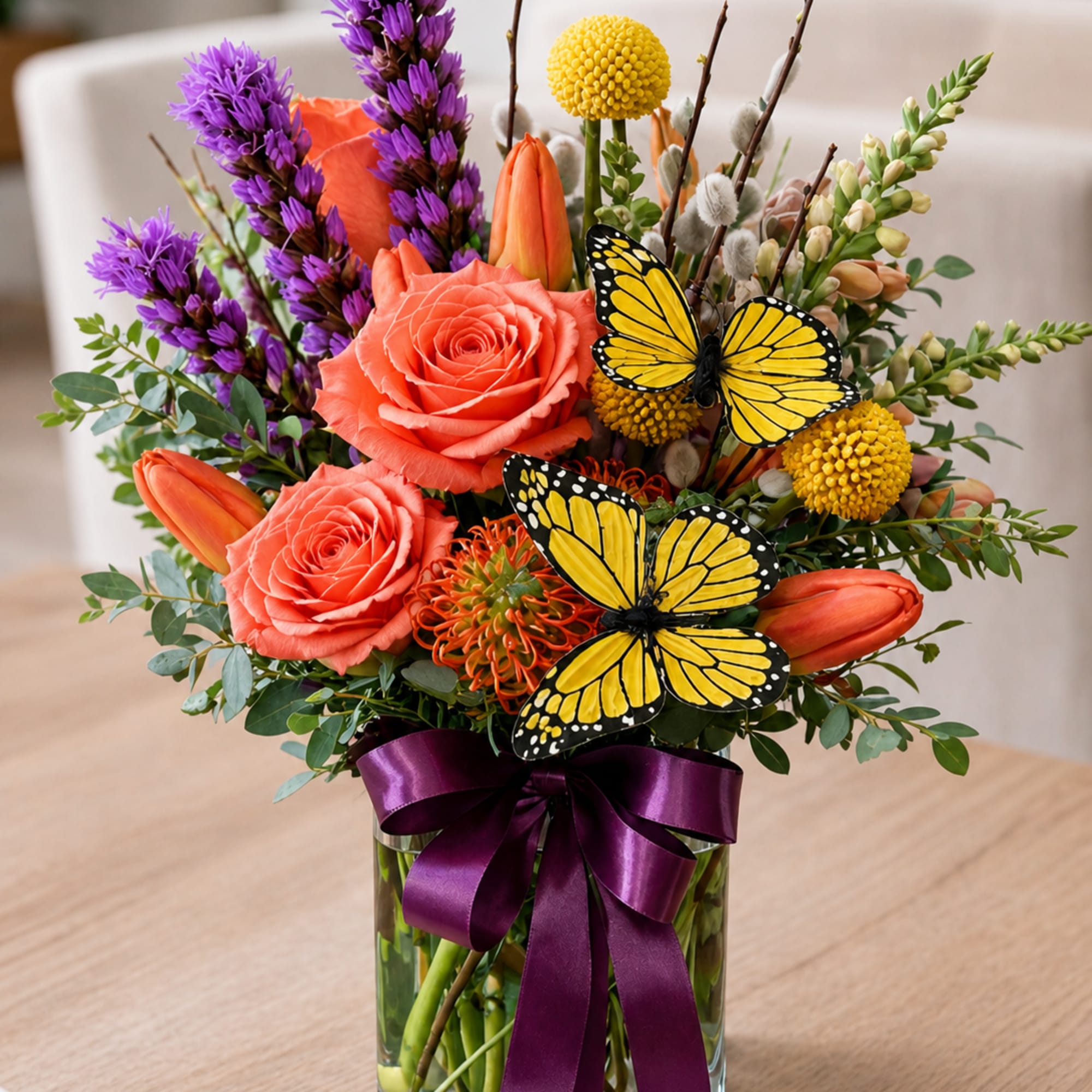 A lush, garden-style flower arrangement featuring roses, tulips, seasonal blooms, and decorative