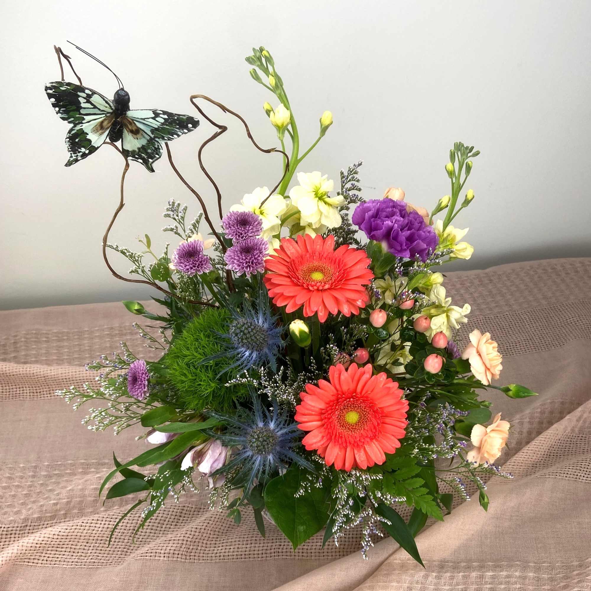 Bright coral gerbera daisies take center stage in this pastel garden-style flower