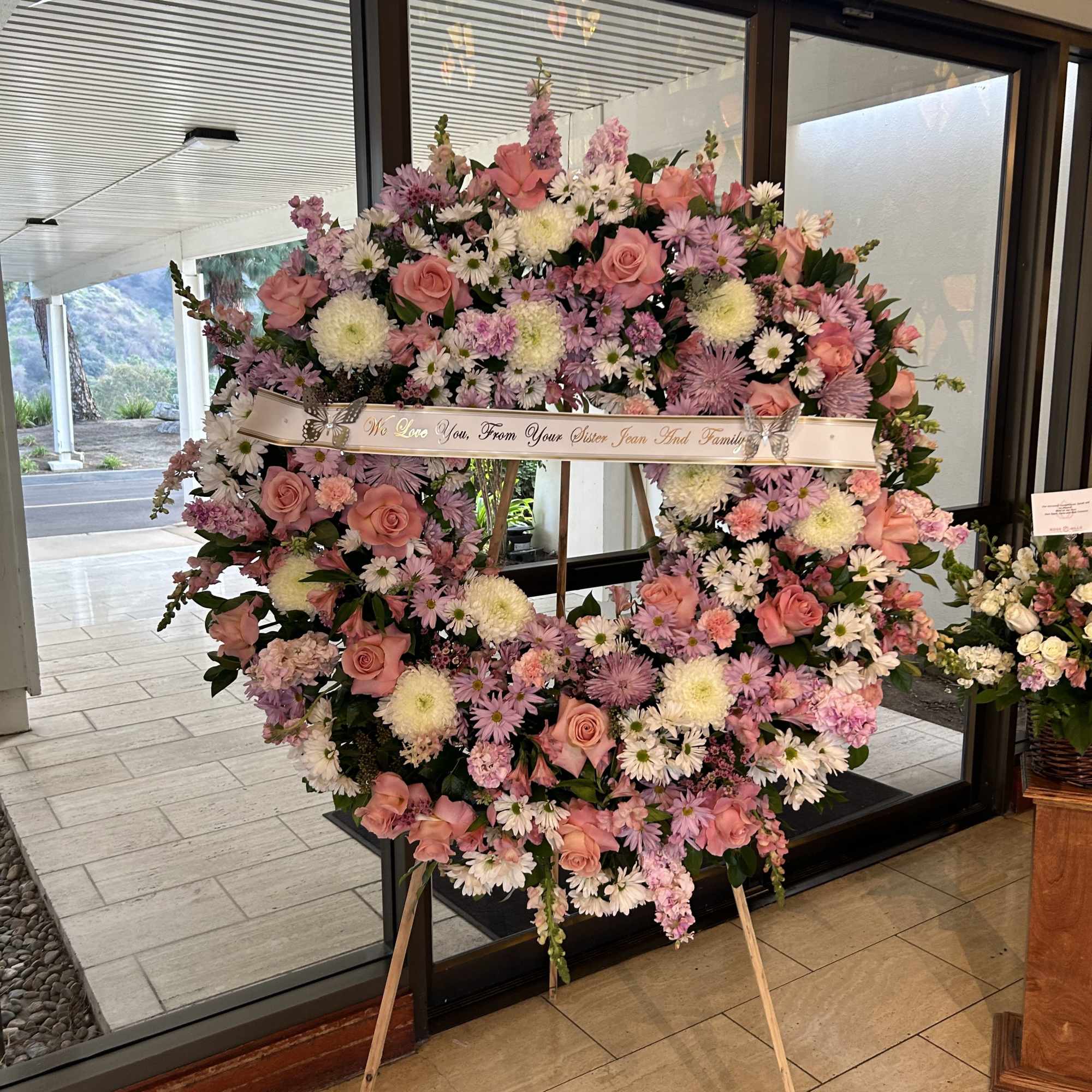 Large pink and white floral wreath on an easel with a memorial ribbon